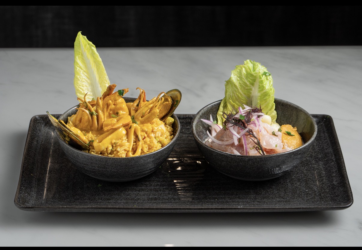 Two bowls of food on a black tray, one with yellow dish and lettuce, the other with pink dish and lettuce