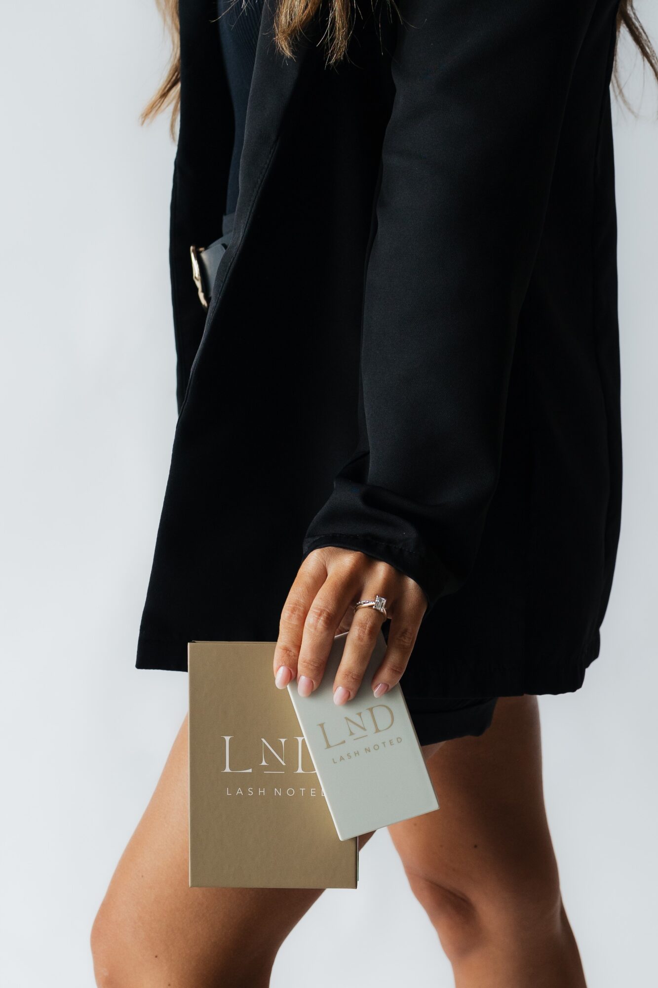Person wearing a black coat holding a beige and white card, with visible hand and part of leg.