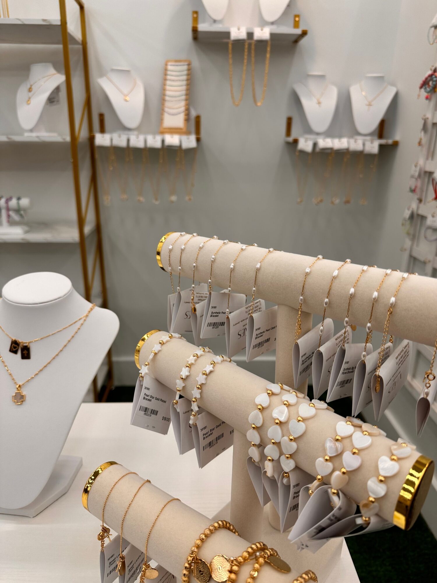 Display of jewelry and accessories on white cylindrical stands, with necklaces and bracelets, in a retail setting.