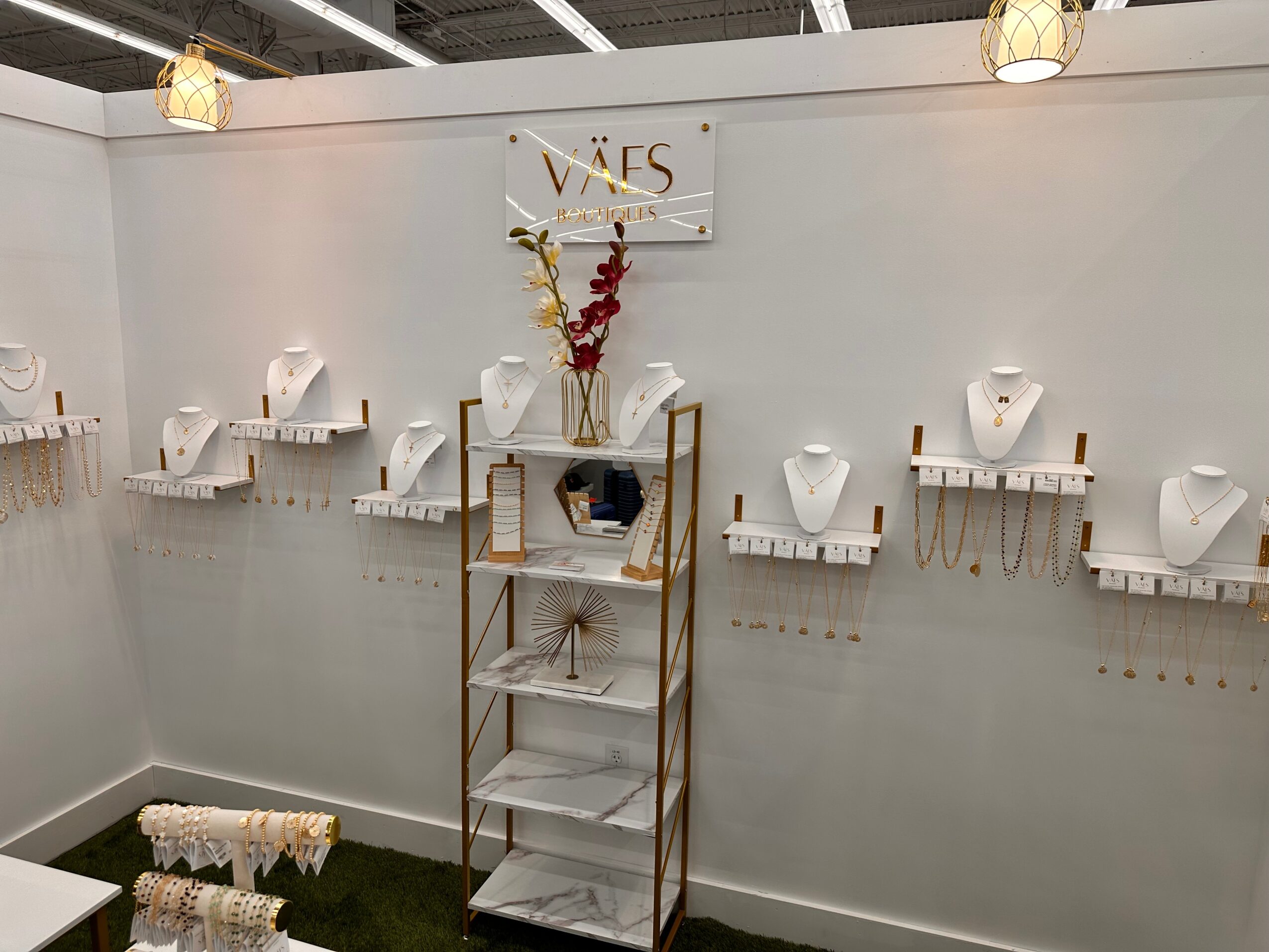 Display of jewelry on white busts mounted on a white wall, with a central shelf holding a vase and decorative items, in a store.