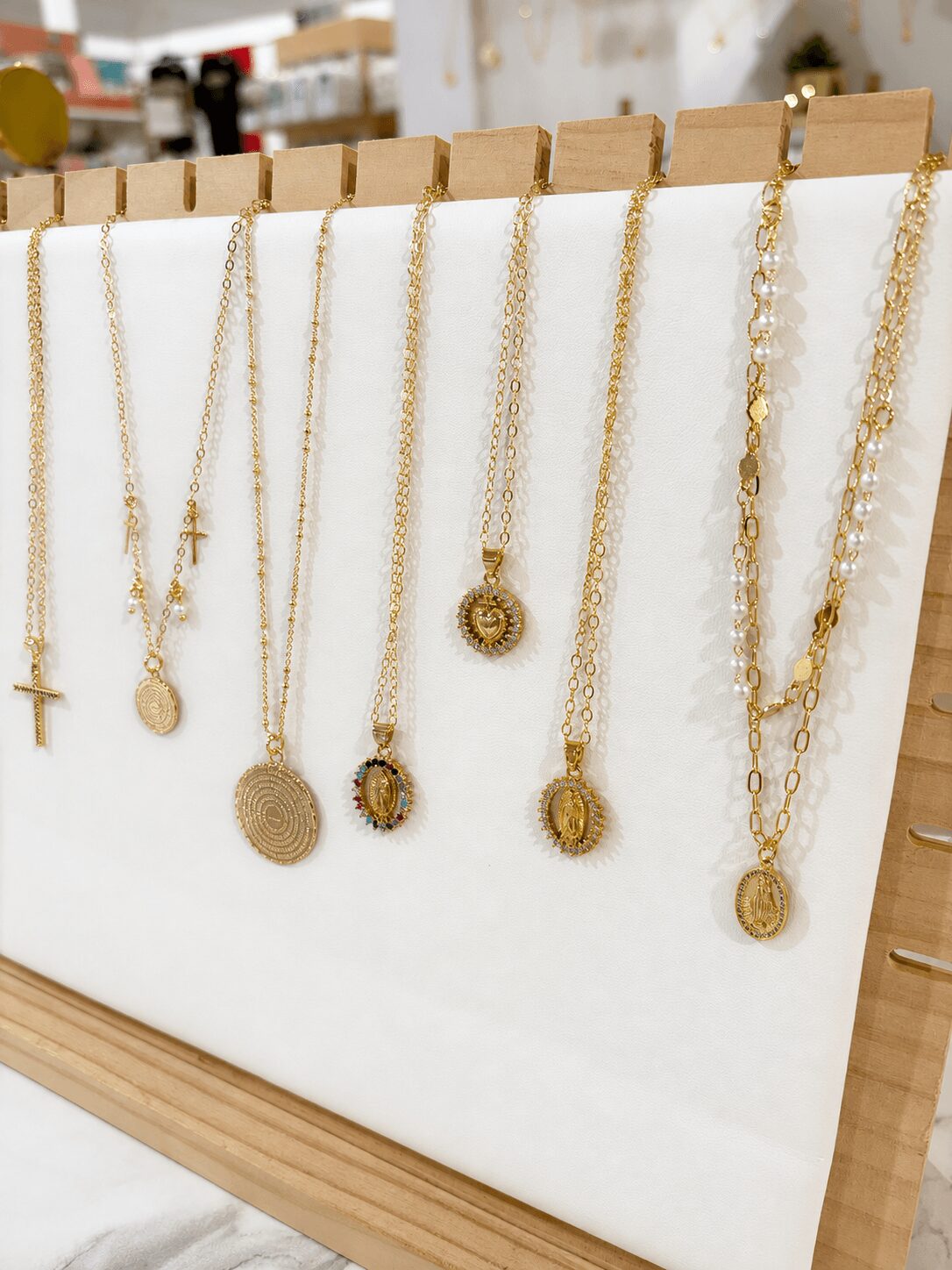 Display of gold necklaces with pendants hanging on a white stand in a store.