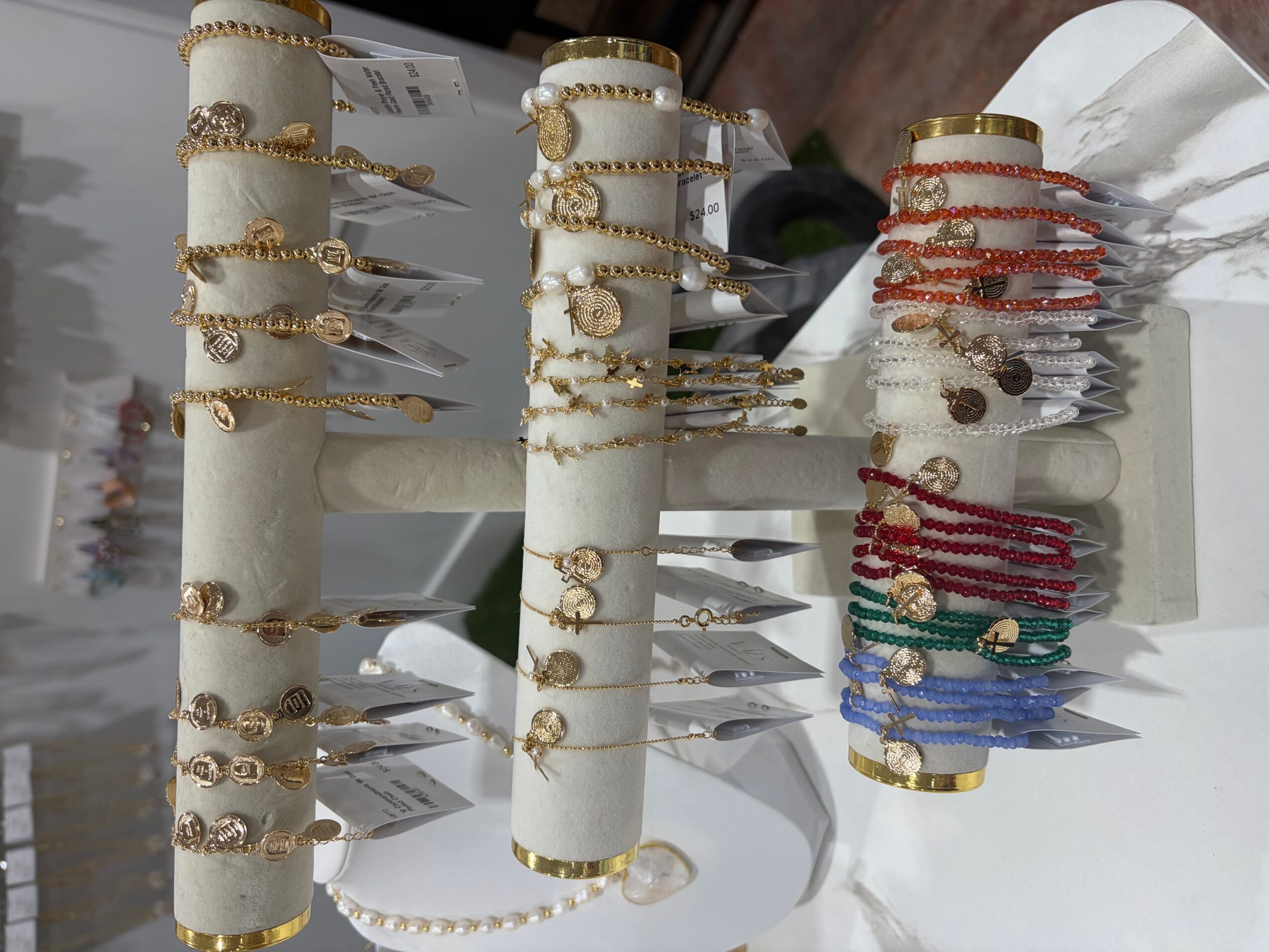 Jewelry display with gold, silver, and colored bracelets on white cylindrical stands, arranged in a retail setting.