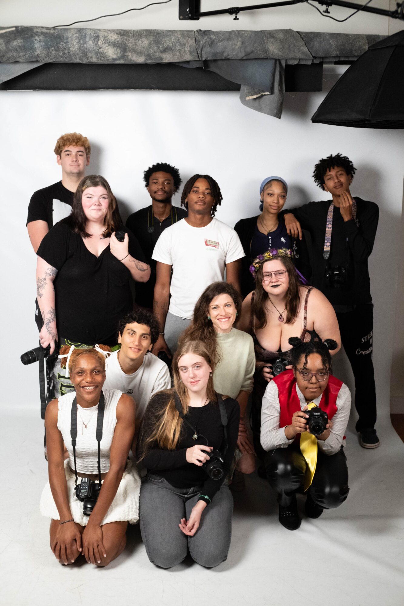 Group of ten diverse people posing in a photography studio with a white backdrop, some smiling and holding cameras.