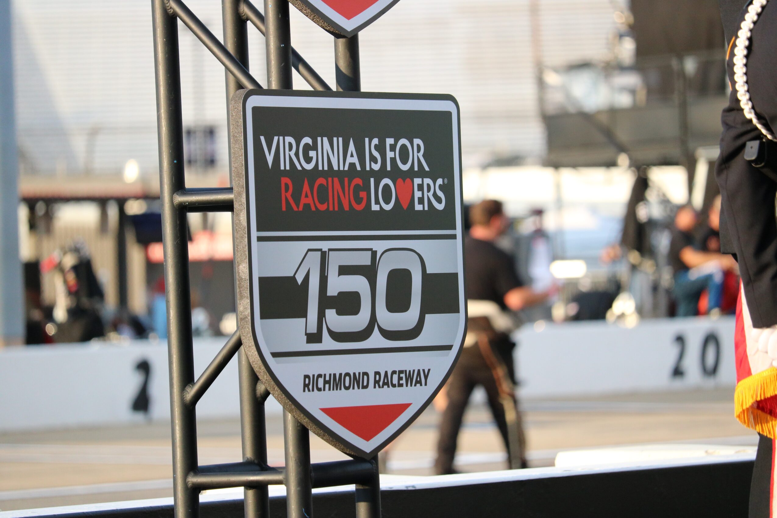 Racing track sign with Virginia and Richmond Raceway text, number 150, and people in the background.