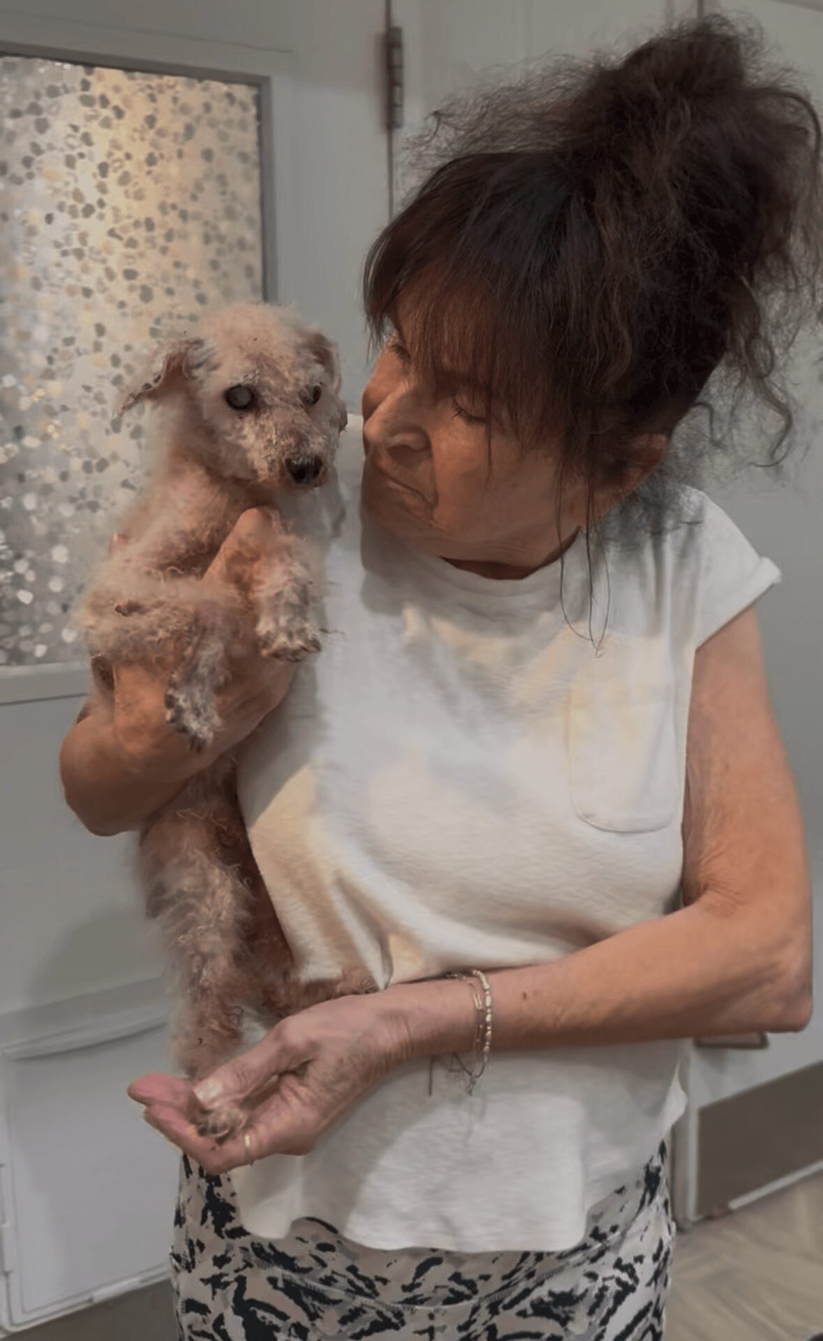 Woman holding a small, curly-haired dog indoors, looking at the dog with a gentle expression.