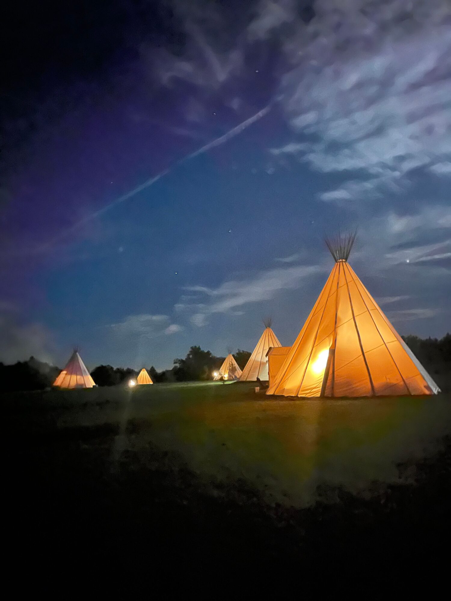 Tents illuminated at night in a grassy area under a partly cloudy sky.