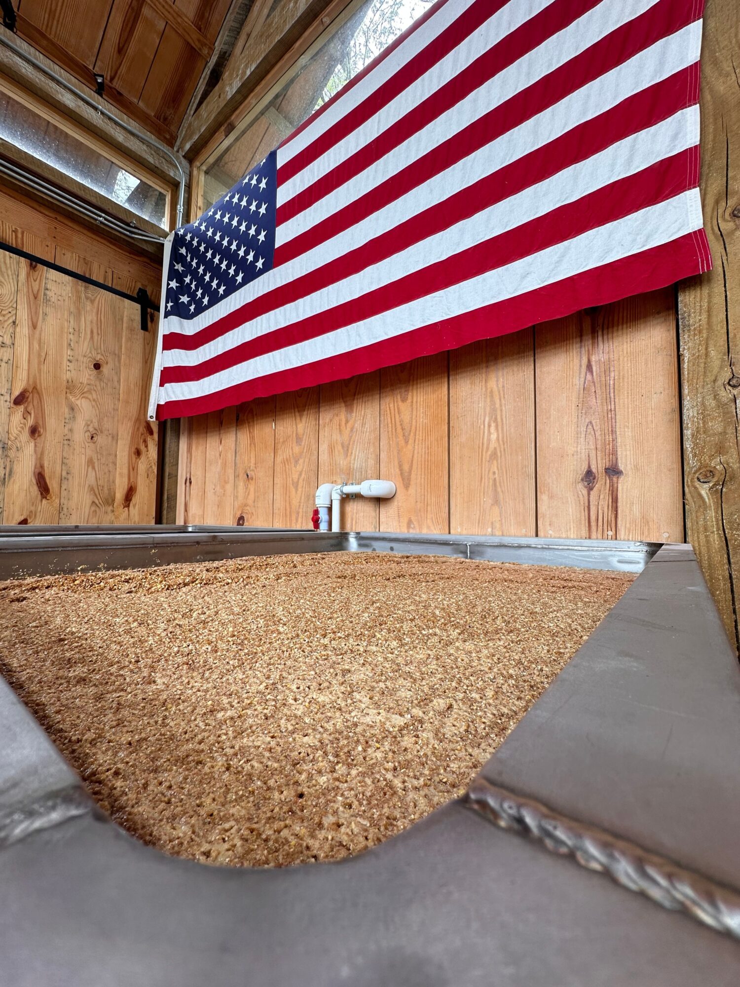 American flag with red and white stripes and blue field with white stars, hanging on a wooden wall.