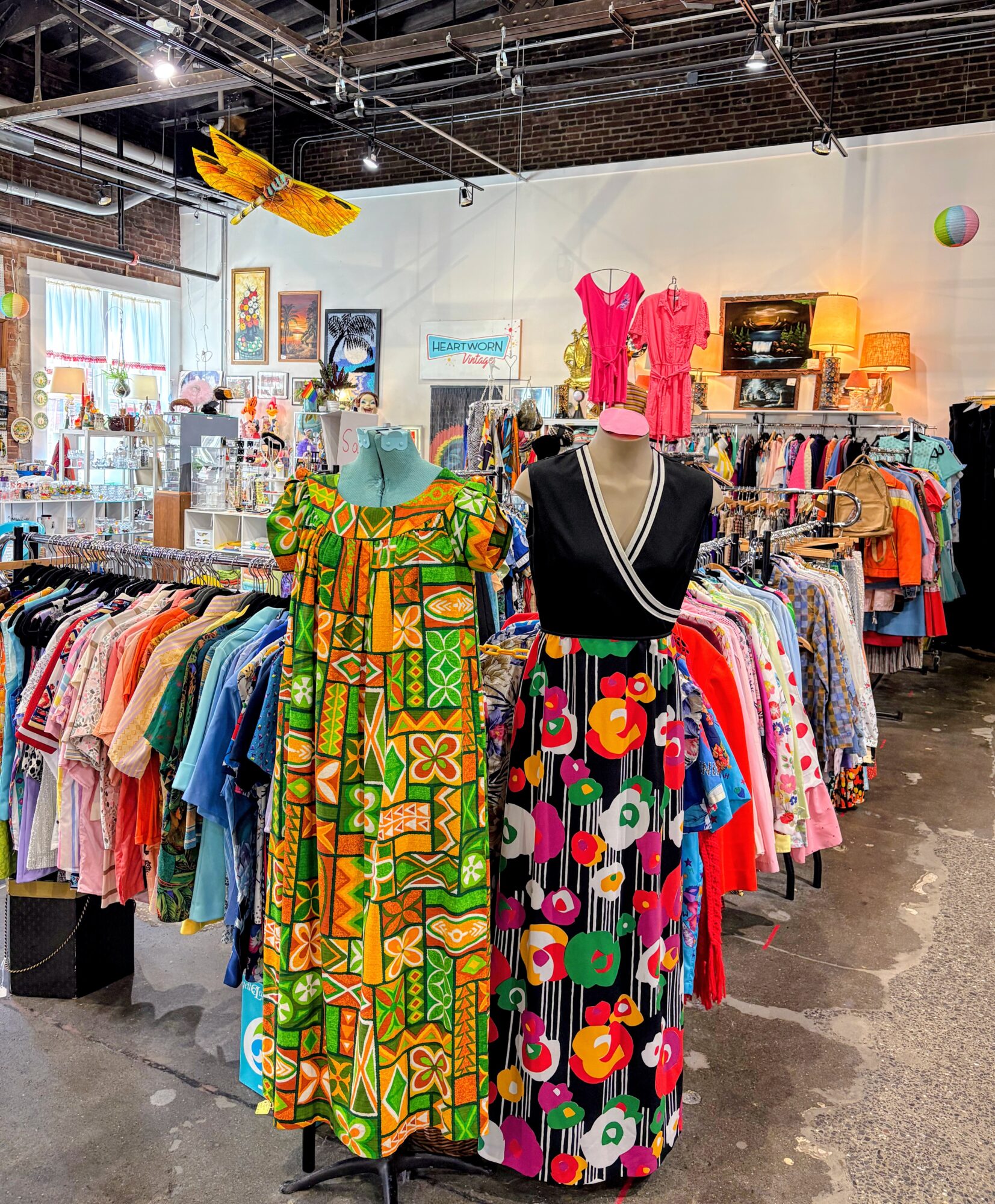 Clothing store with colorful dresses on mannequins and racks, bright lighting, and various accessories in the background.