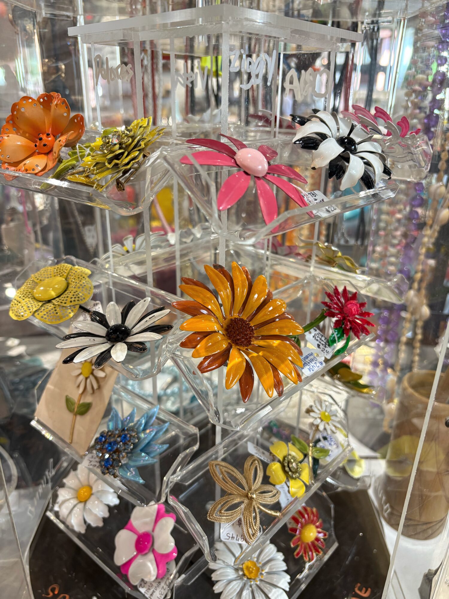 Display of colorful decorative hairpins with flowers and insects on a transparent stand.