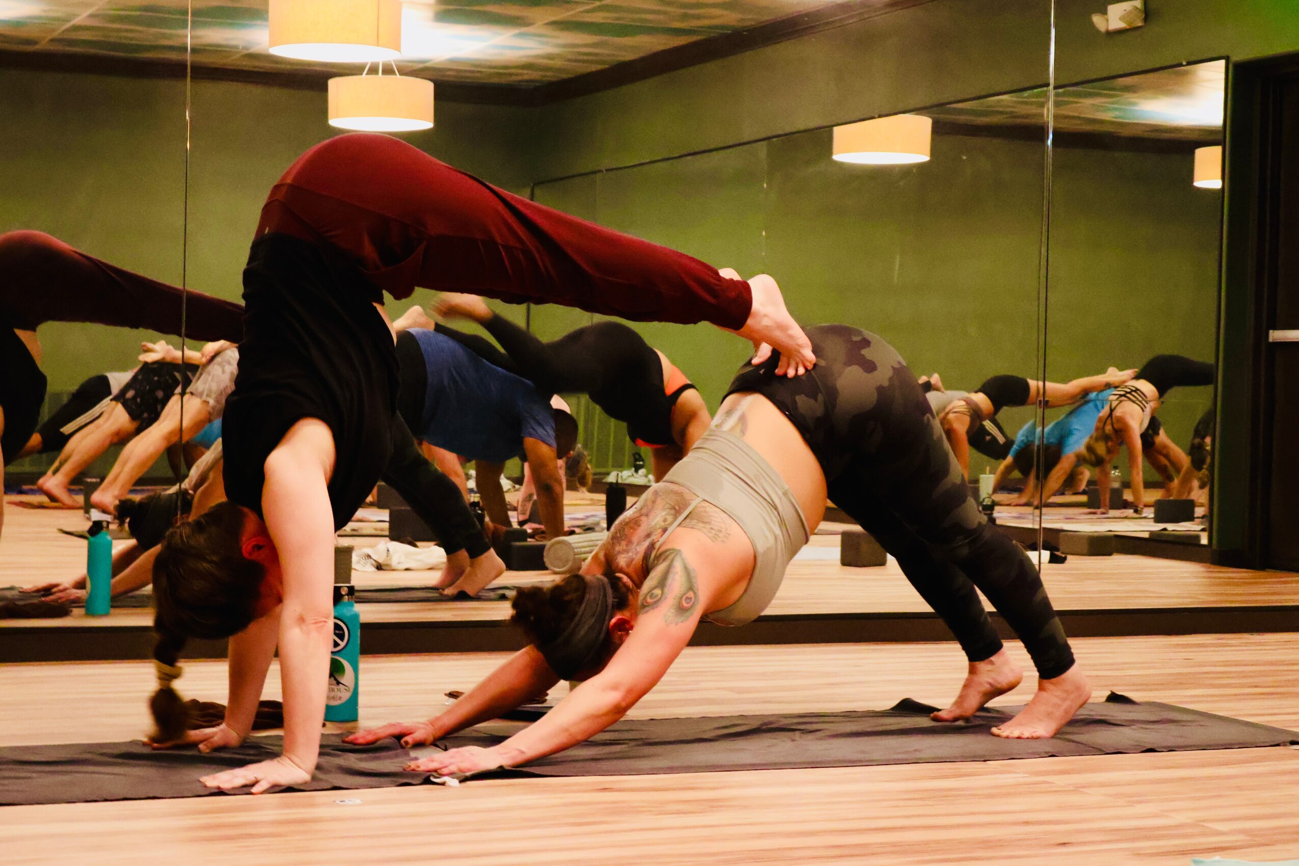 People practicing yoga in a studio, performing downward dog pose with mirrors on the wall behind them.