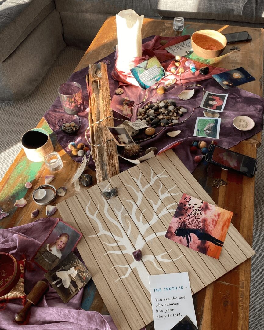 Messy table with various items including bowls, cups, photographs, and decorative objects, with a wooden board and a small painting.
