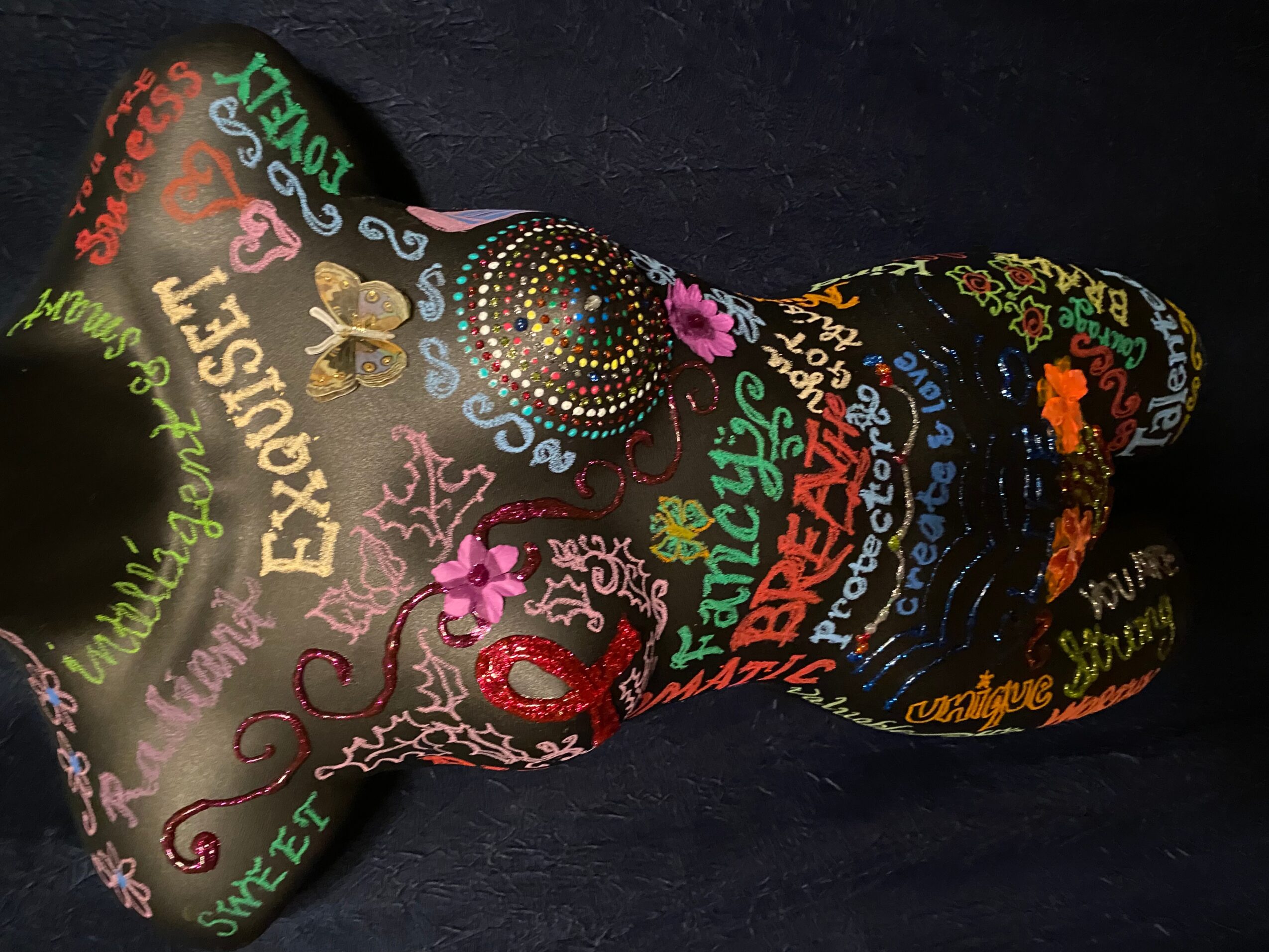 Colorful, decorated guitar with various words and designs, including flowers and patterns, on a dark background.