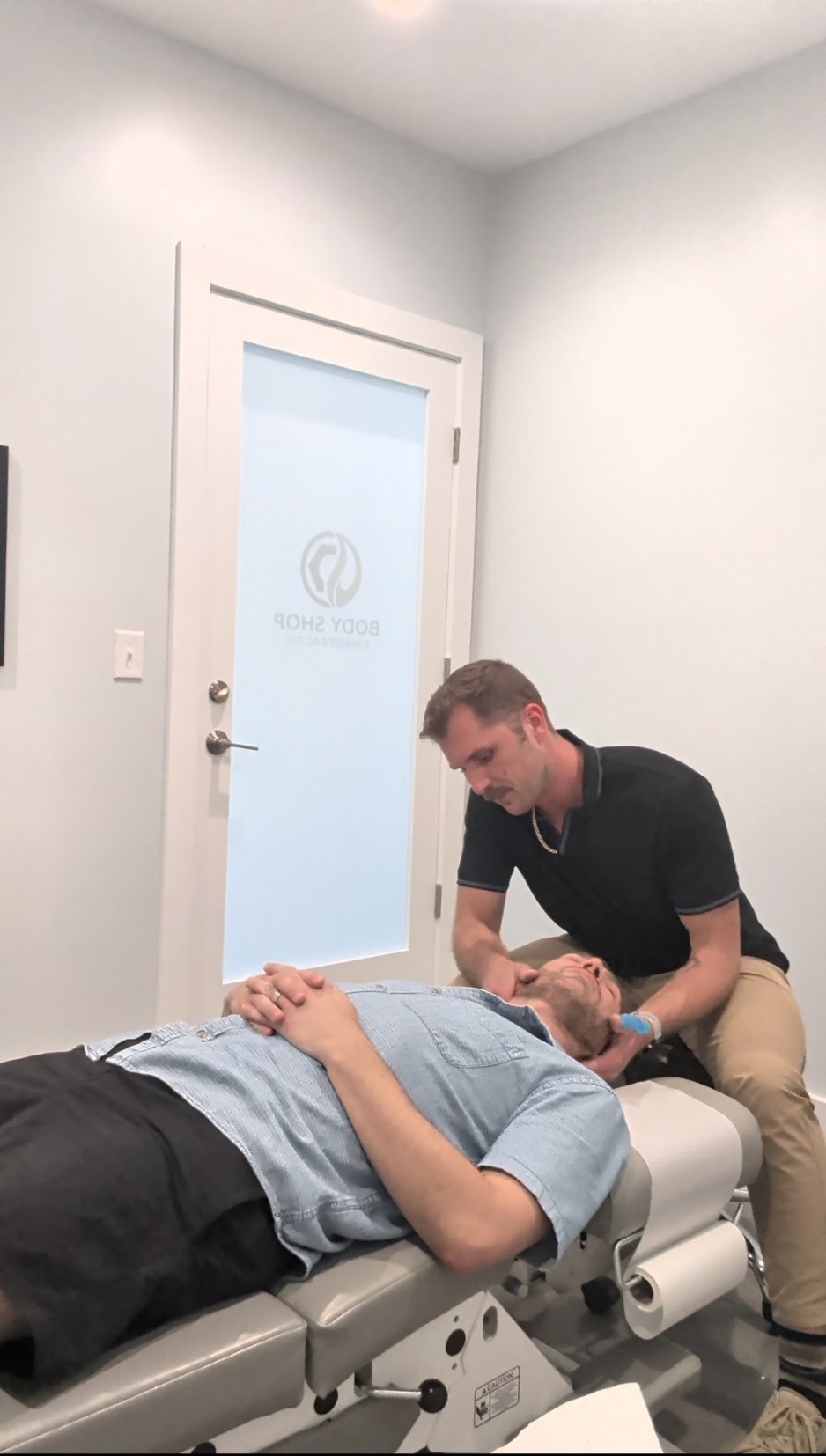 Person lying on a medical examination table with another person attending to them in a clinical room.