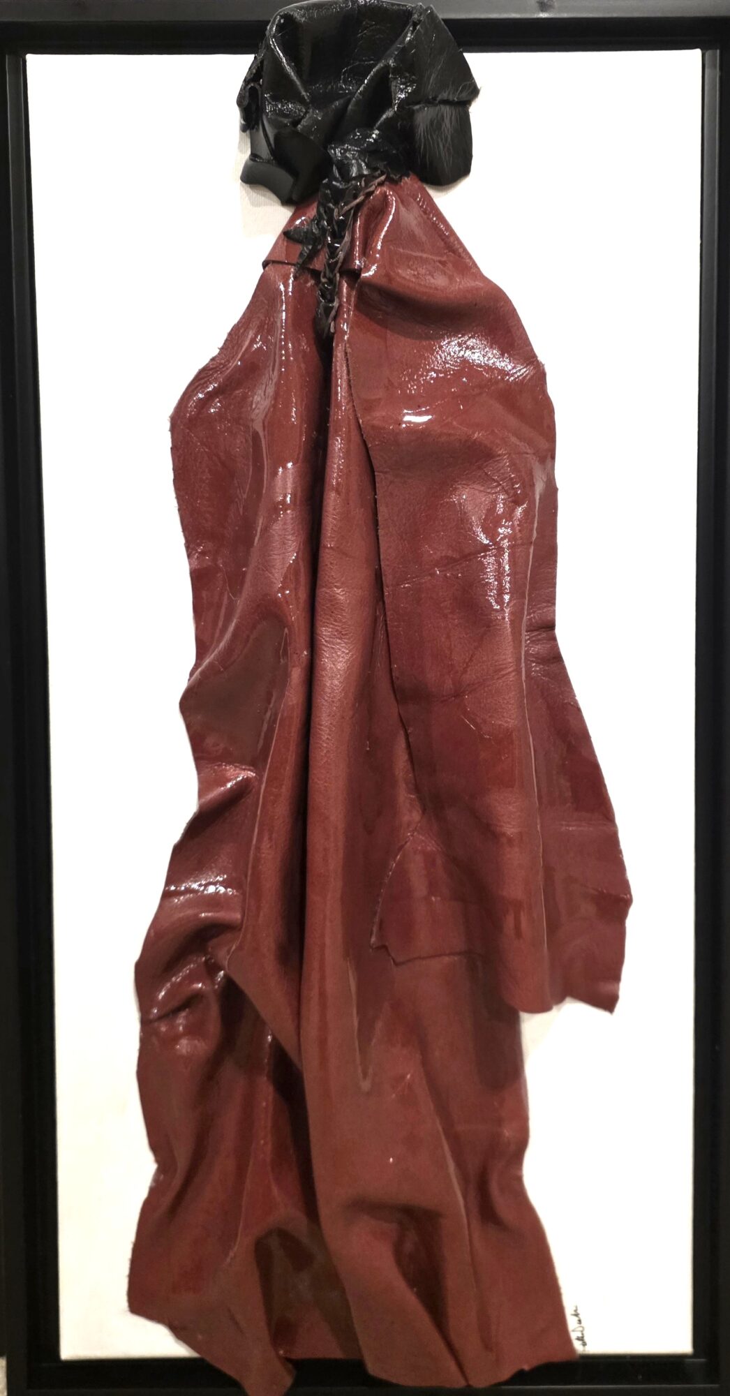 A red, shiny, crumpled garment hanging on a black hook against a white background.