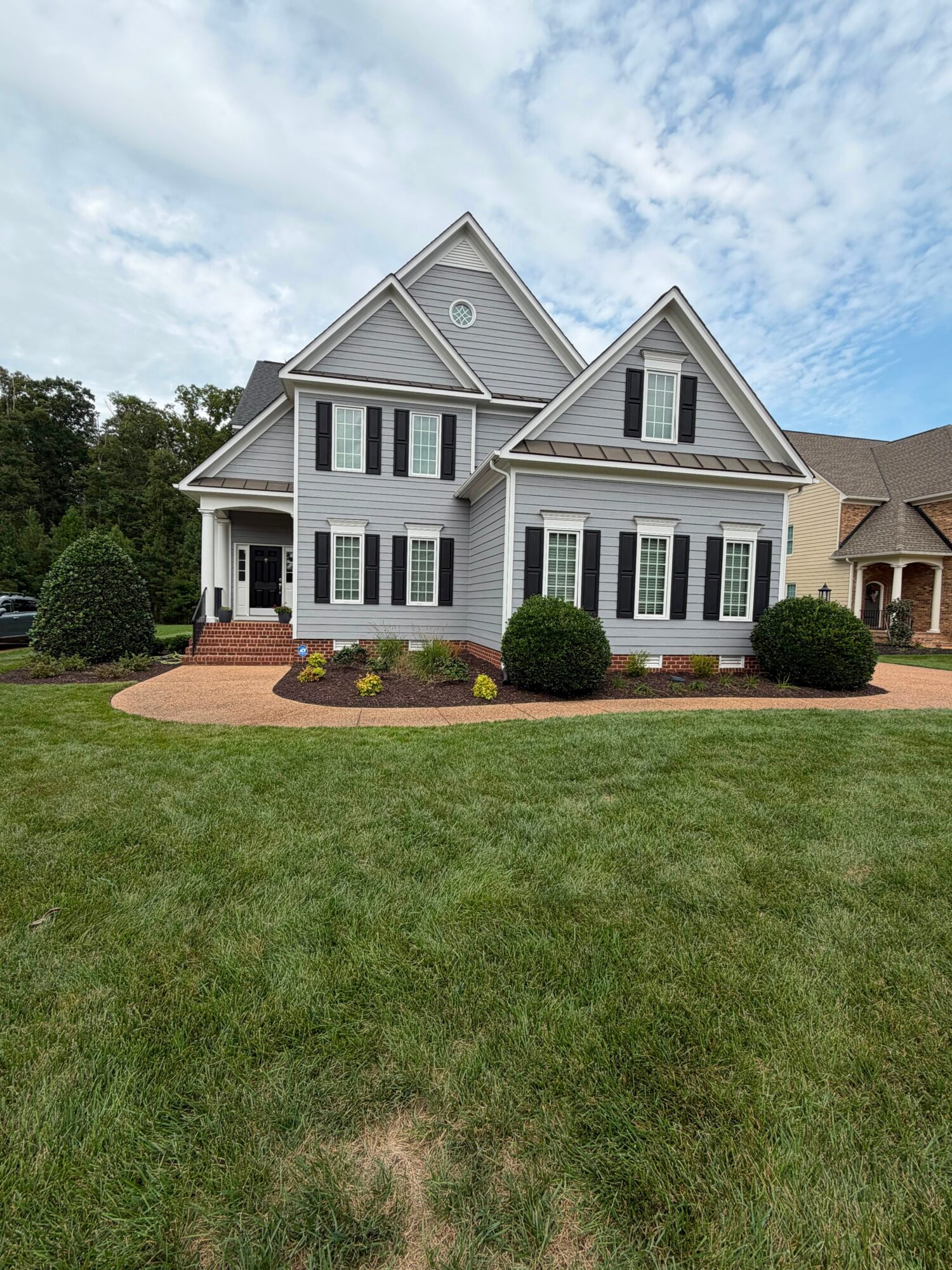 Large white house with multiple gabled roofs, black shutters, and a front porch, surrounded by a green lawn and landscaping.