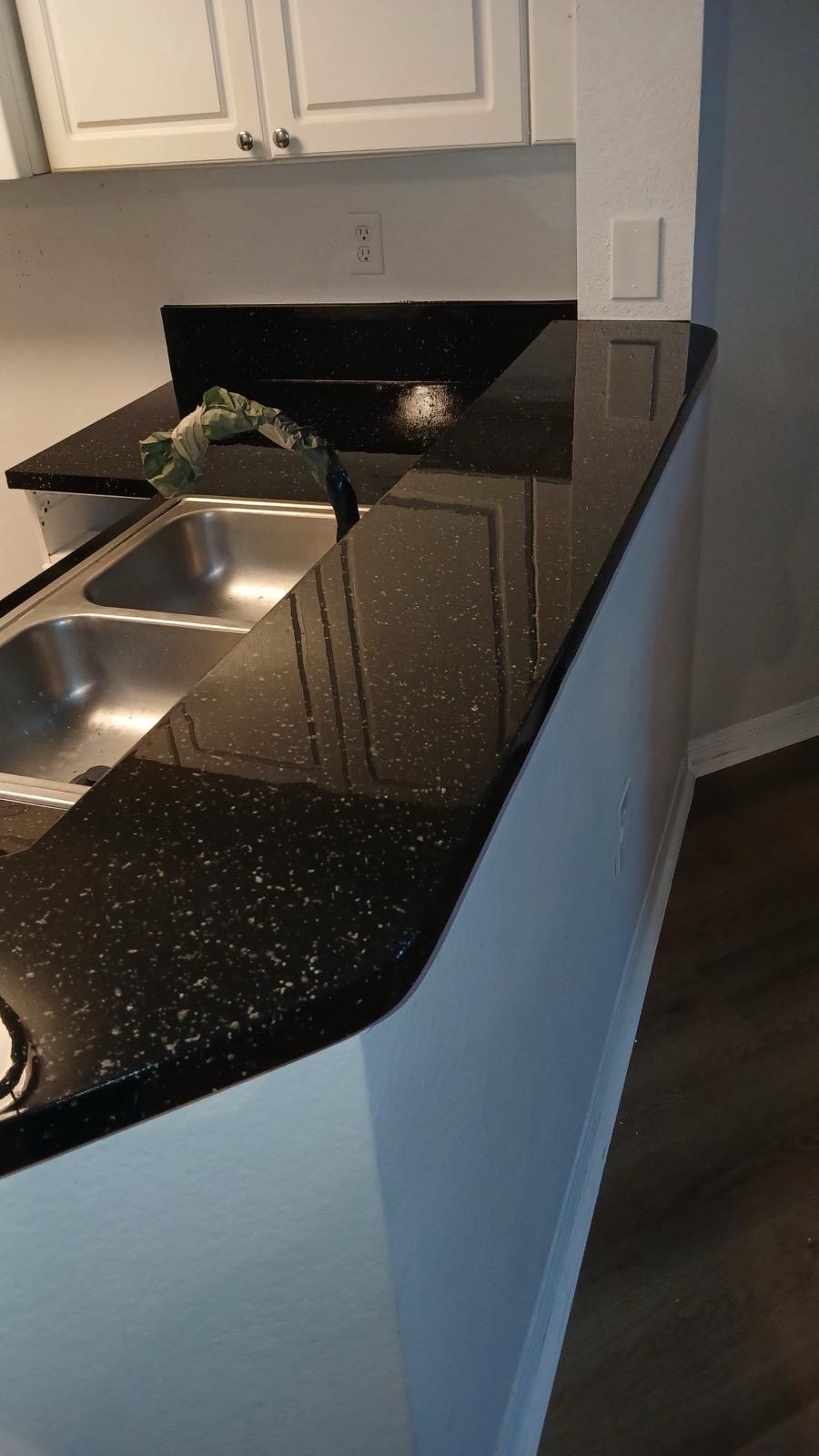 Black granite kitchen countertop with a sink and faucet, white cabinets above, and a dark floor below.