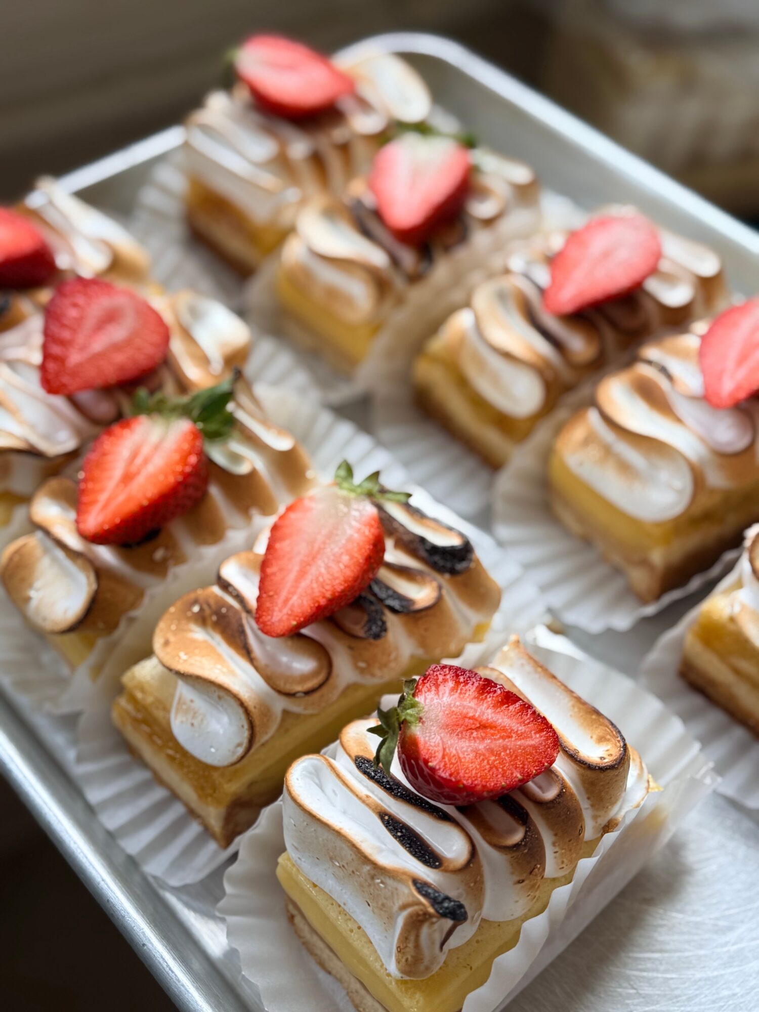Assorted small rectangular desserts topped with strawberries, almonds, and chocolate, arranged on a white tray.
