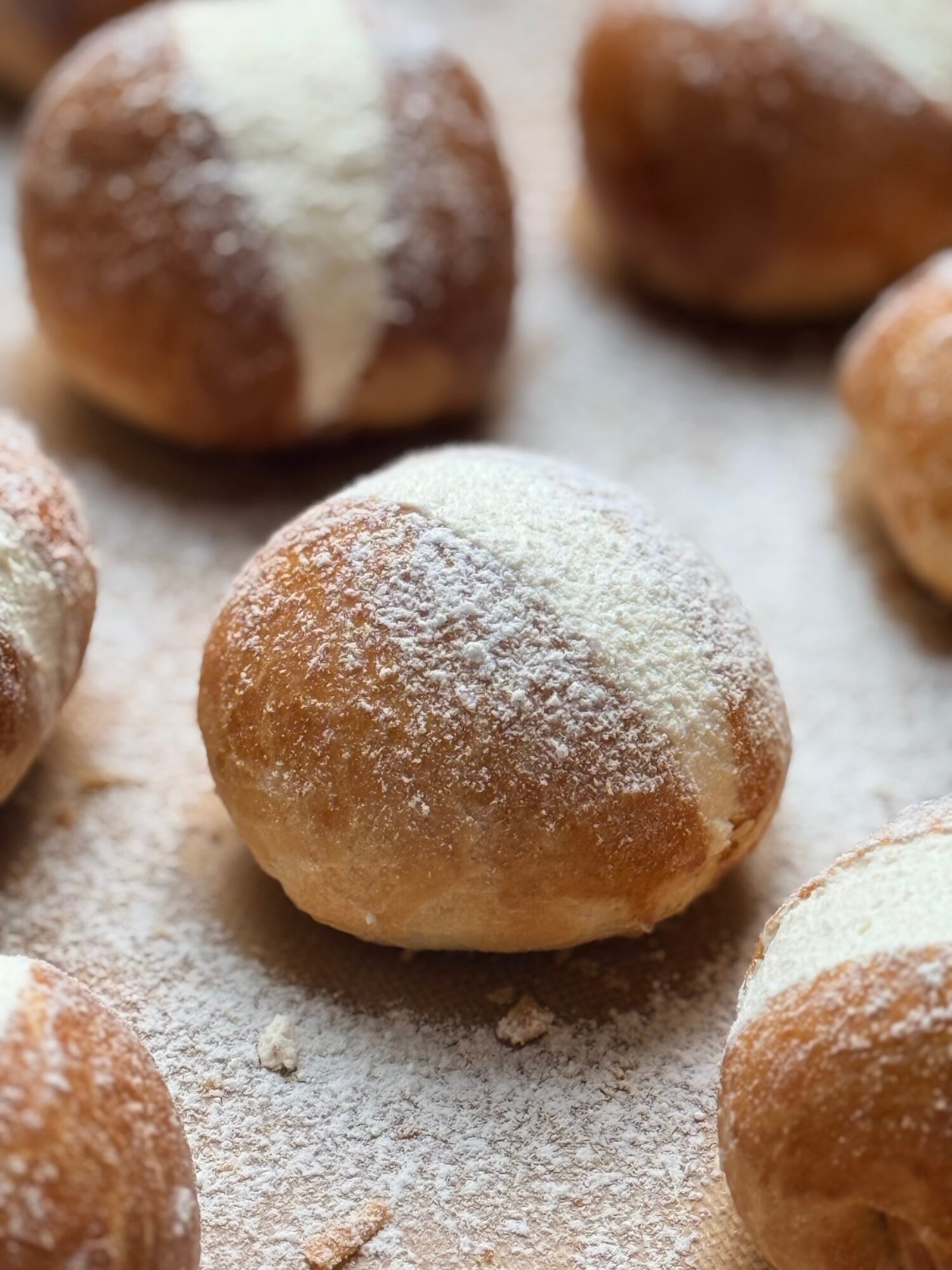 Round pastry dusted with powdered sugar on a surface with other similar pastries nearby.