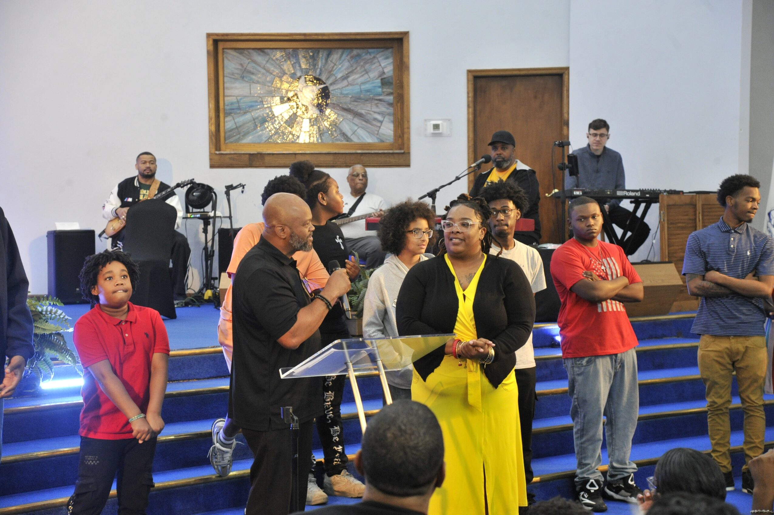 Group of people on stage with musical instruments and a large abstract artwork in the background.