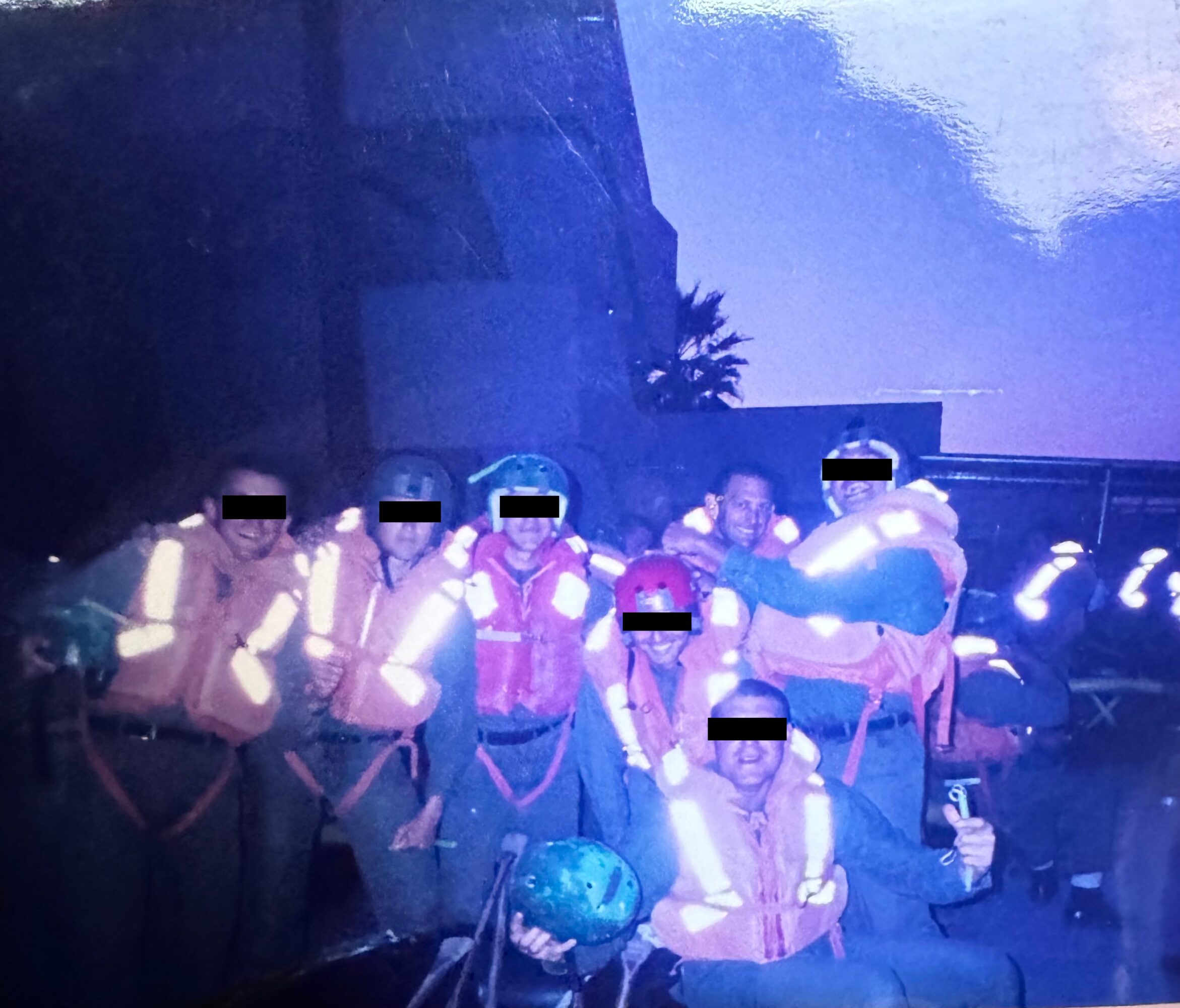 Group of people wearing reflective vests, some holding a ball, outdoors during dusk or dawn, with buildings and sky in background.