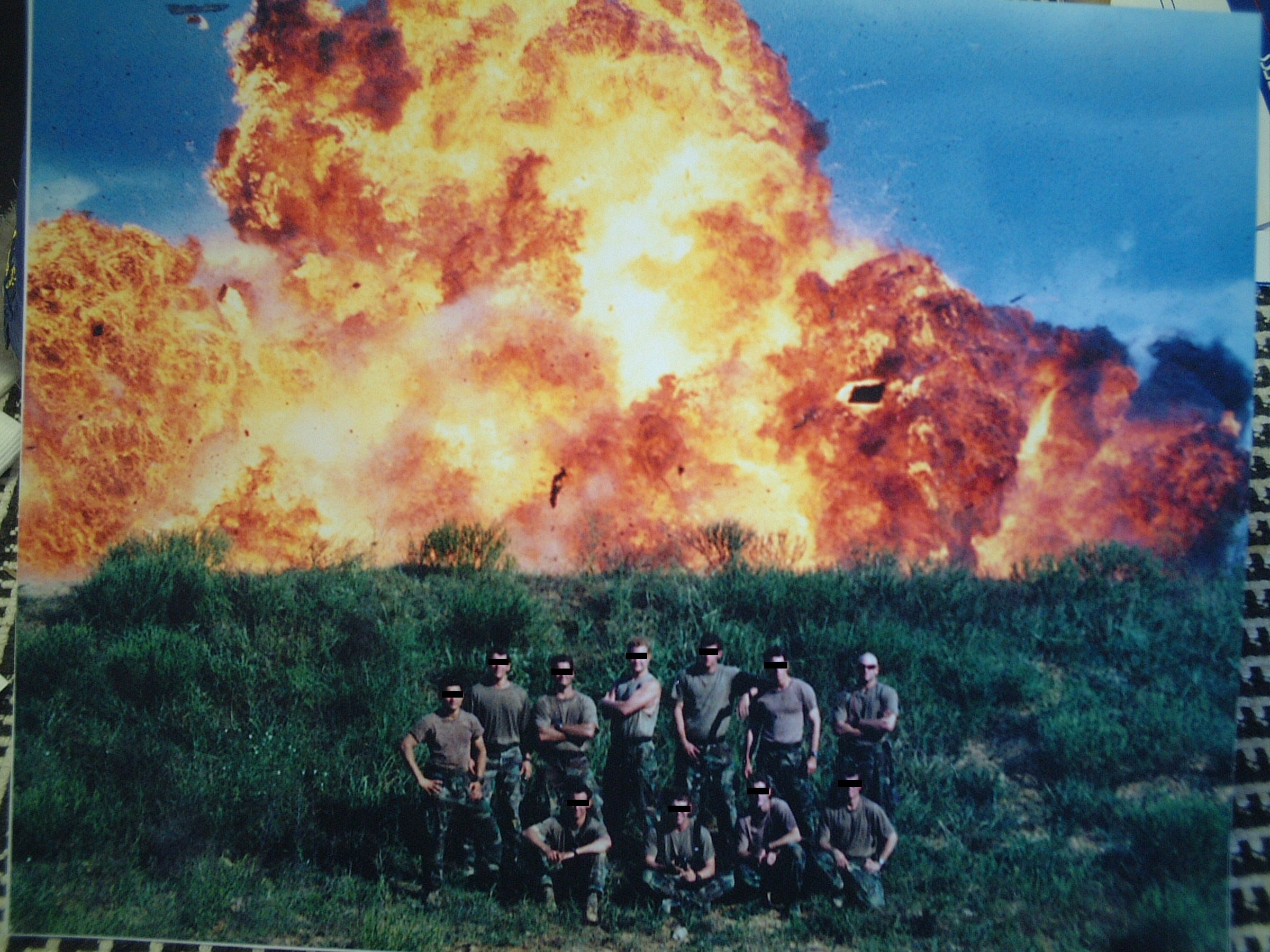 Group of people standing in front of large explosion with fire and smoke in the background.