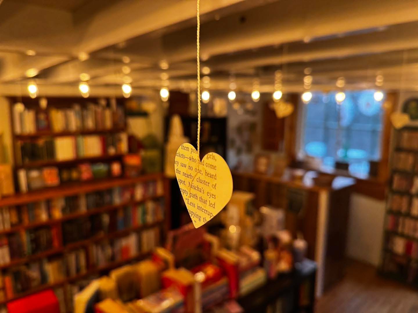 Heart-shaped paper hanging from string in a cozy bookstore with bookshelves and warm lighting