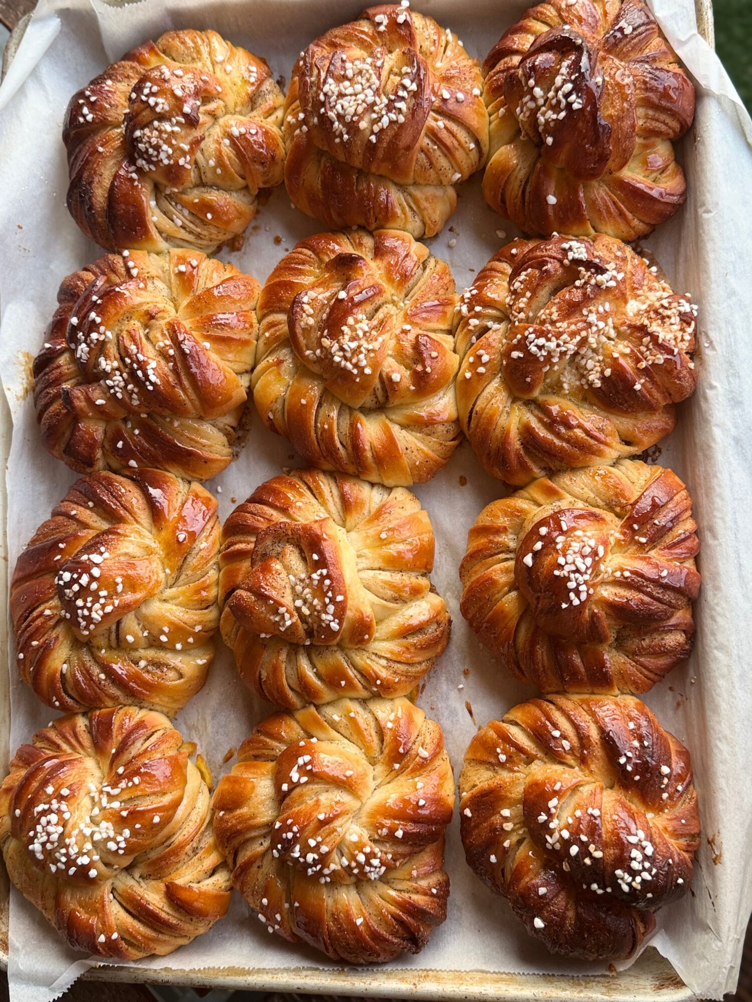 Twelve freshly baked croissants with sugar crystals on top, arranged on parchment paper in a baking tray.