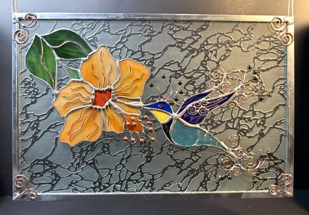 Decorative stained glass panel with a yellow flower, green leaves, and a blue hummingbird, set against a textured background.
