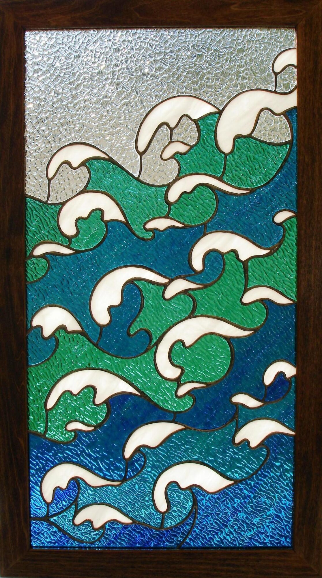 Stained glass window depicting stylized ocean waves with white foam, green and blue water, and a cloudy sky.