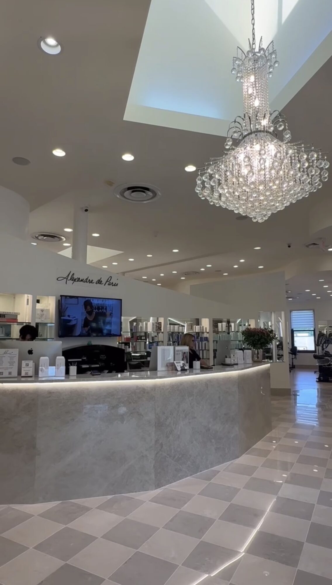 Elegant interior with a chandelier, reception desk, and check-in area, featuring a high ceiling and modern decor.
