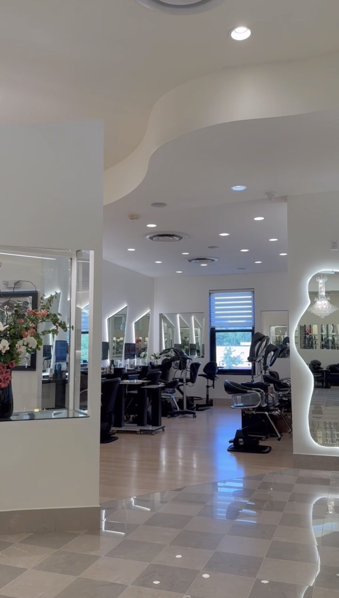 Modern salon interior with chairs, mirrors, and large windows, bright lighting, and a curved ceiling design.
