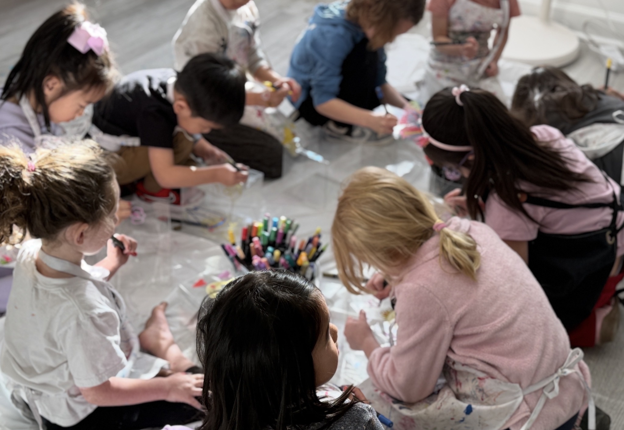 Children gathered around a table with colorful markers, engaging in a creative activity indoors.