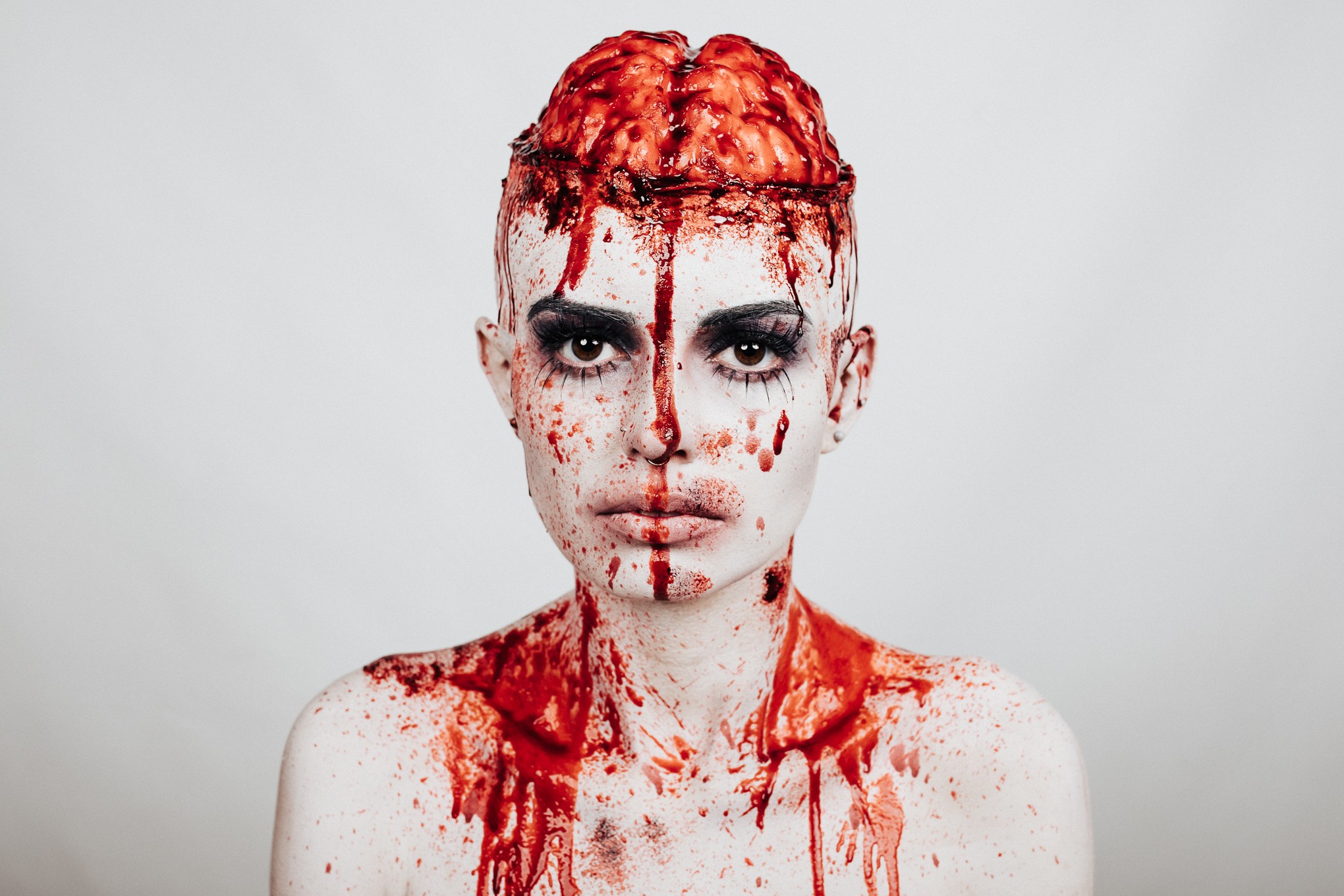 Person with red hair and face covered in red paint or substance, looking directly at the camera, neutral expression.