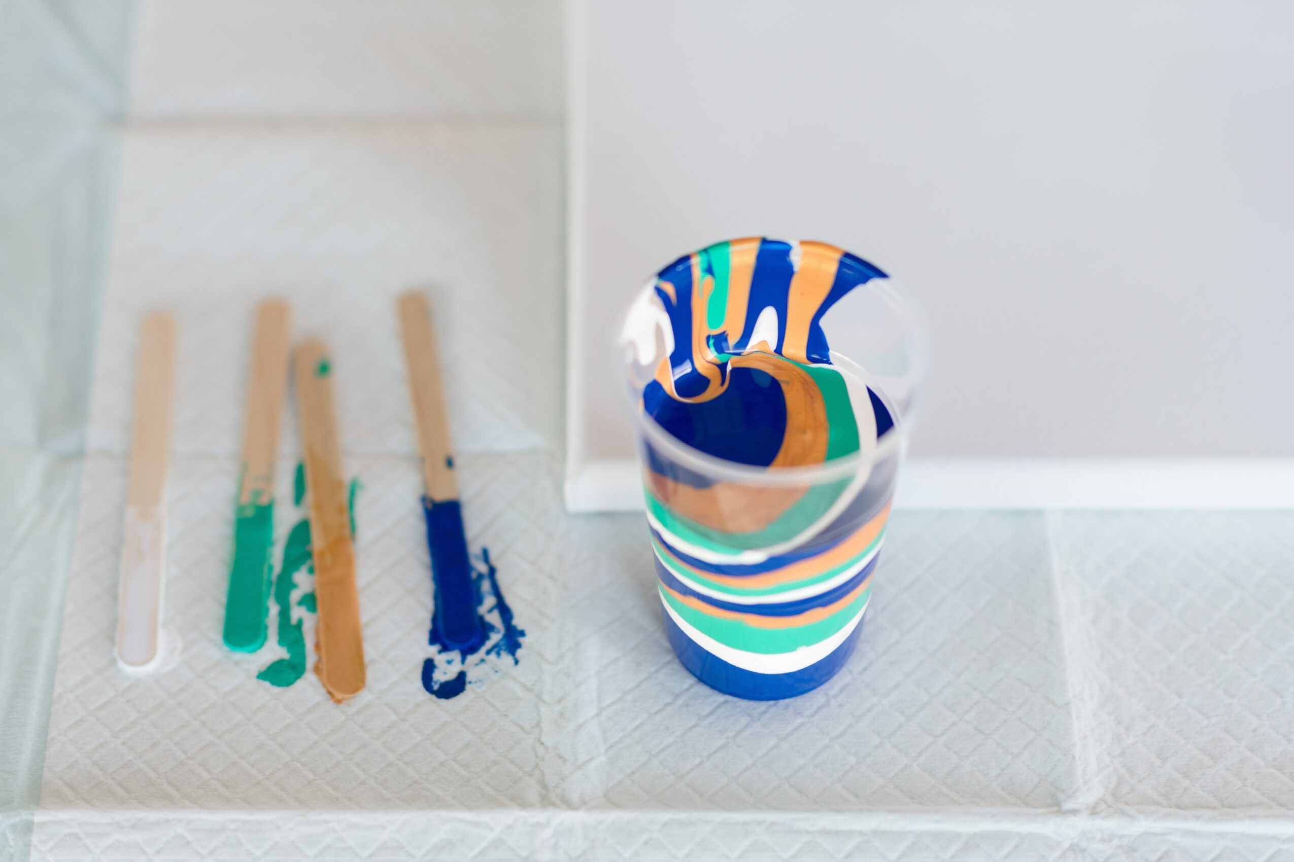 A colorful striped cup with a marbled pattern on a white surface, with paint swatches nearby.