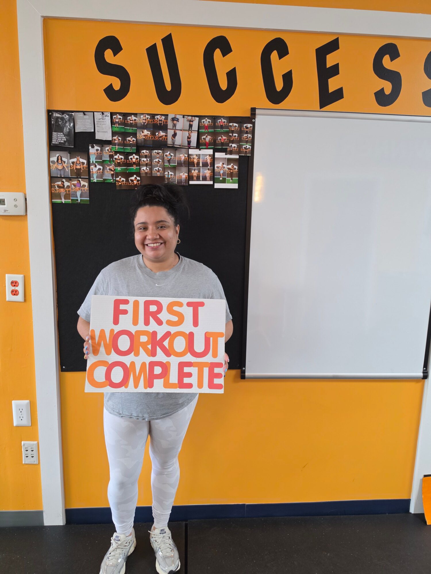 Person standing in front of a wall with a whiteboard and shelves, wearing a shirt with text, in a room with orange and black walls.