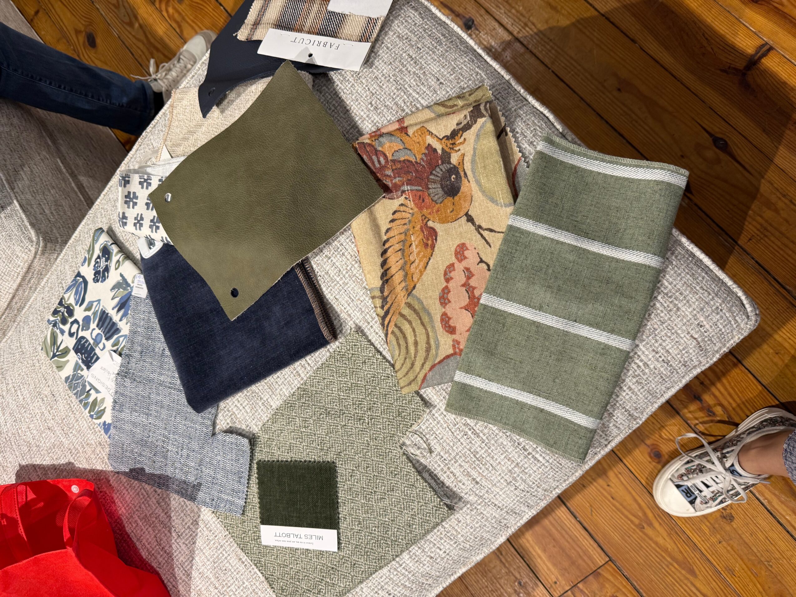 Various fabric swatches and a book on a table with a wooden floor and a person's shoe visible.