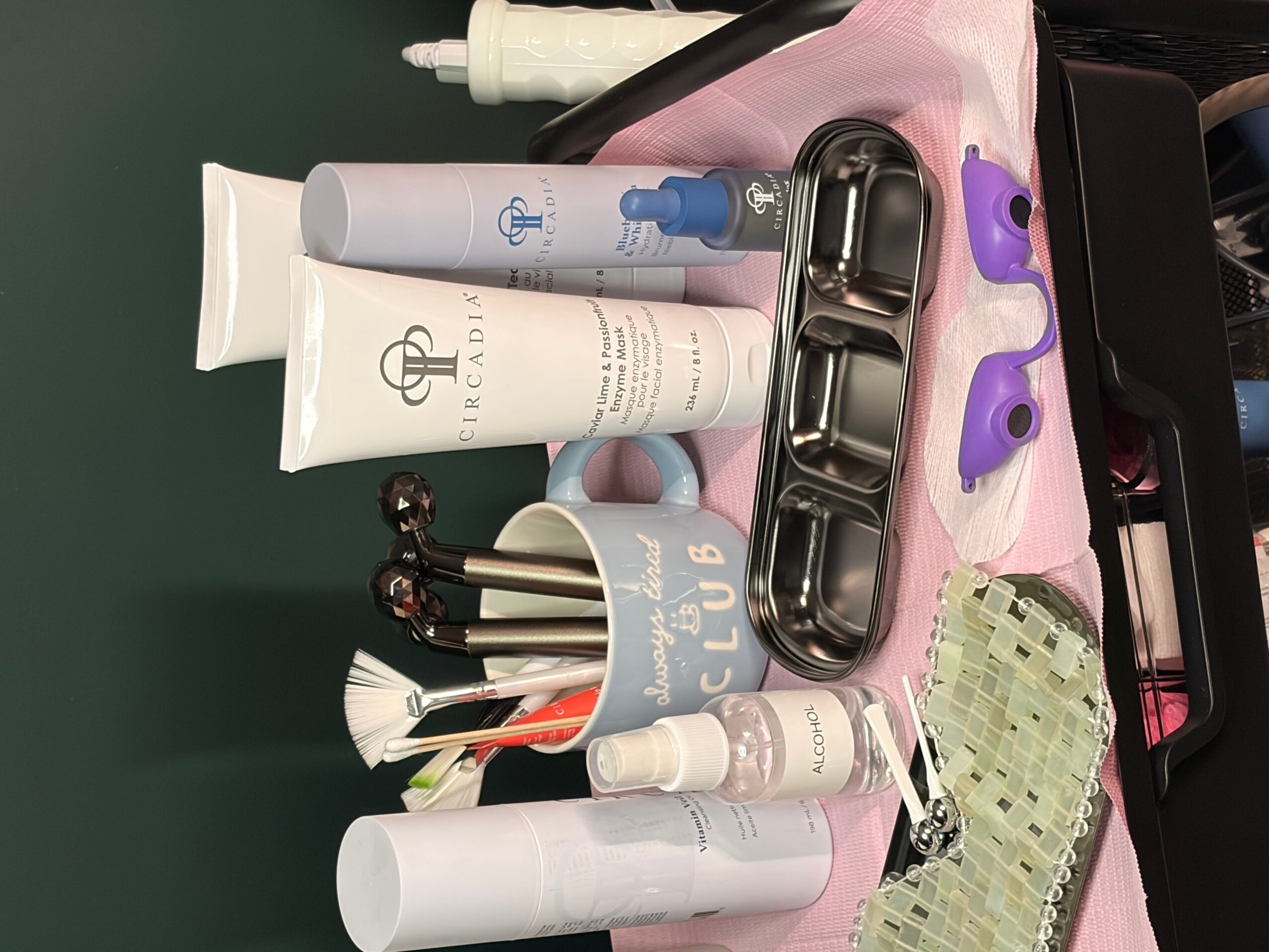 Collection of personal care items including tubes, bottles, earbuds, and a container with cotton swabs on a pink cloth.