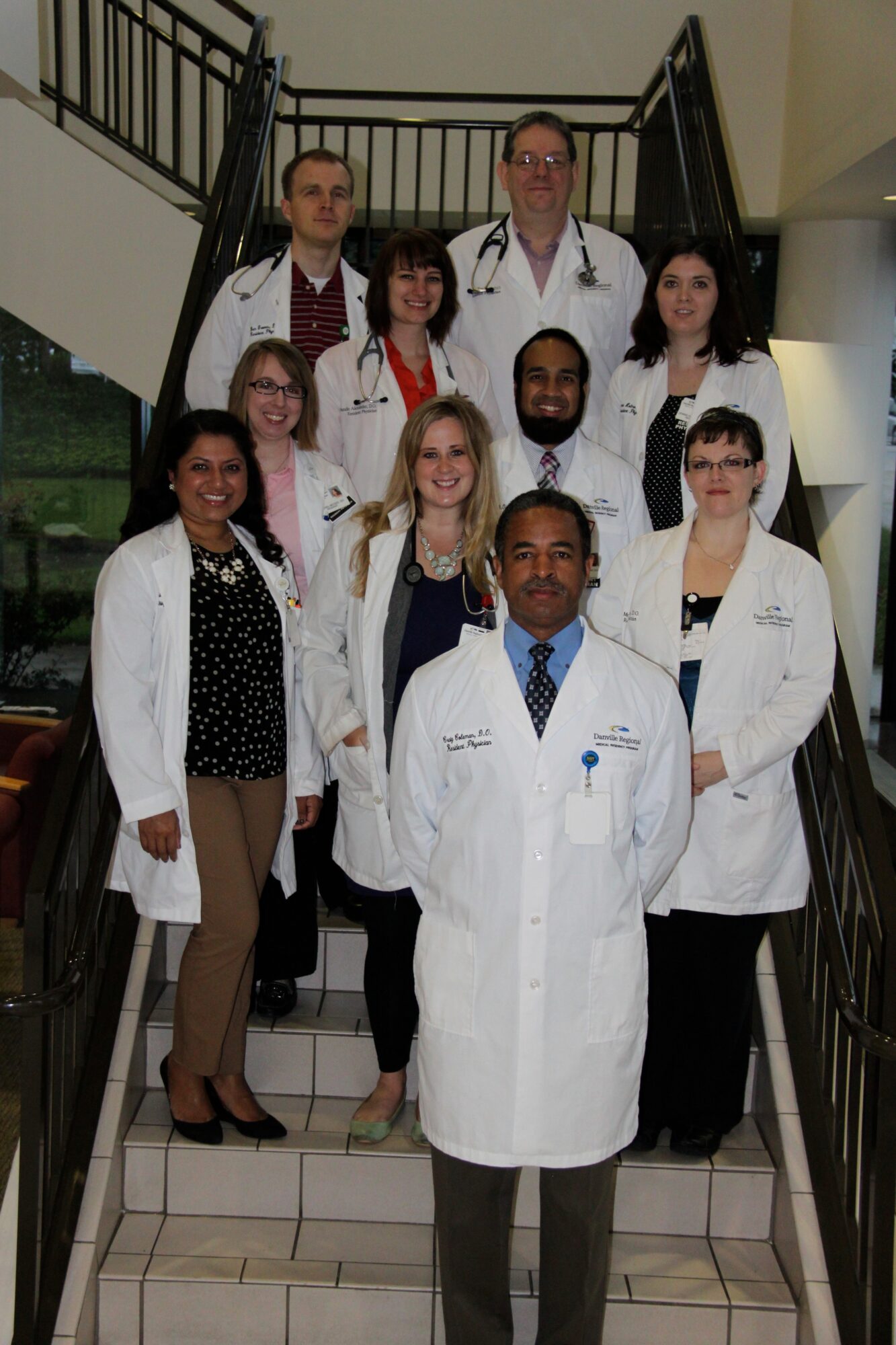 Group of ten medical professionals in white coats standing on staircase indoors.