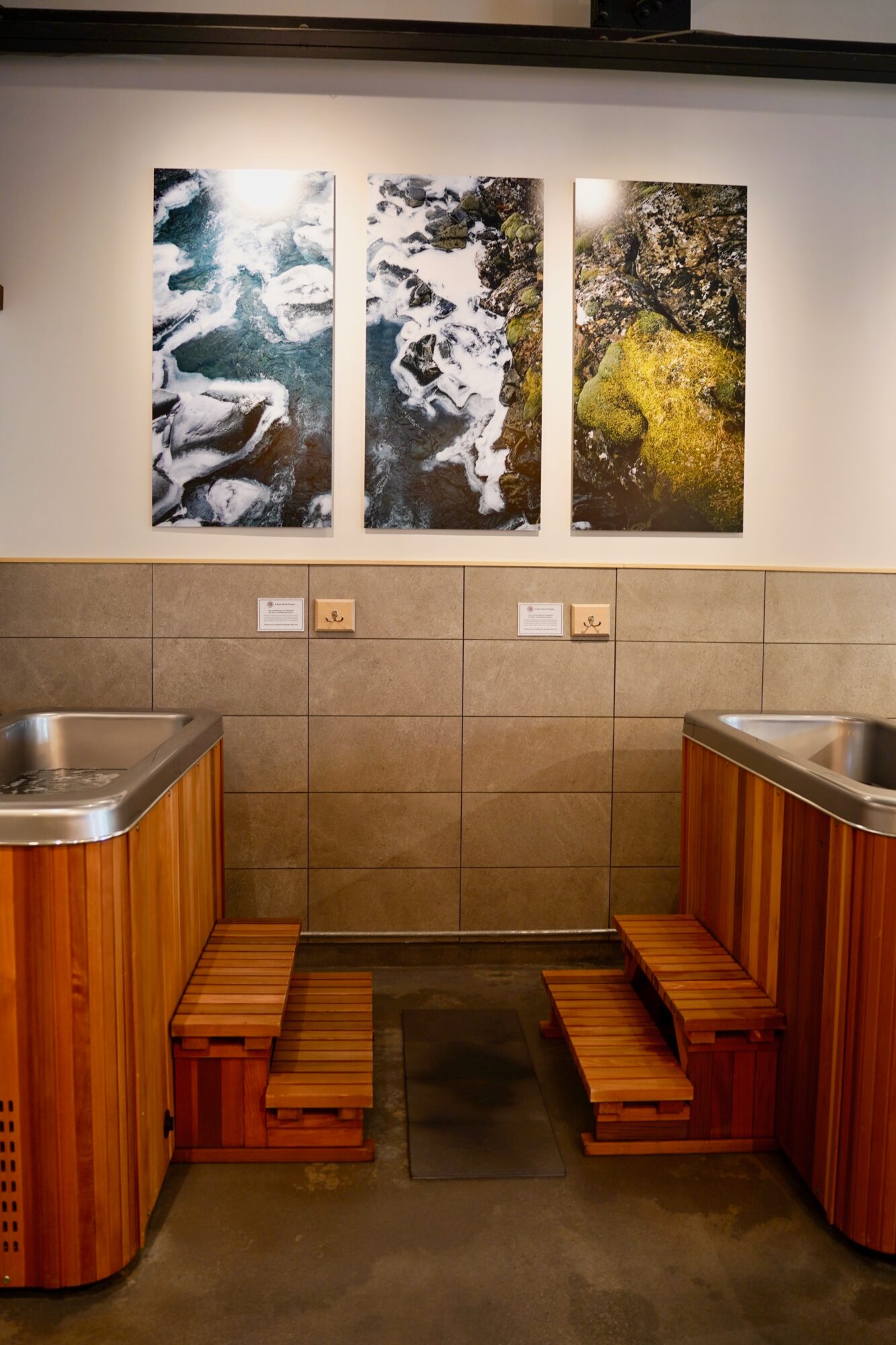 Three vertical landscape paintings on a wall above a tiled area with wooden benches and sinks.
