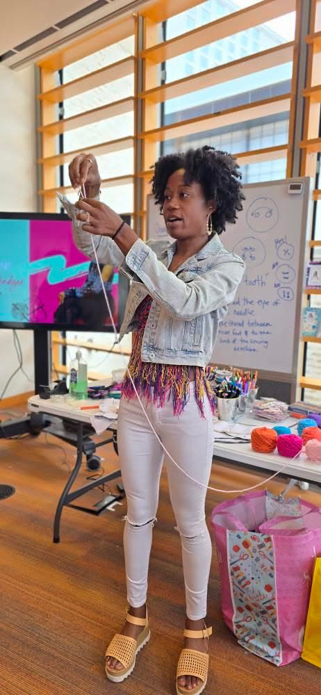 Woman holding a skull model in a classroom with a whiteboard and colorful supplies, large windows in the background.