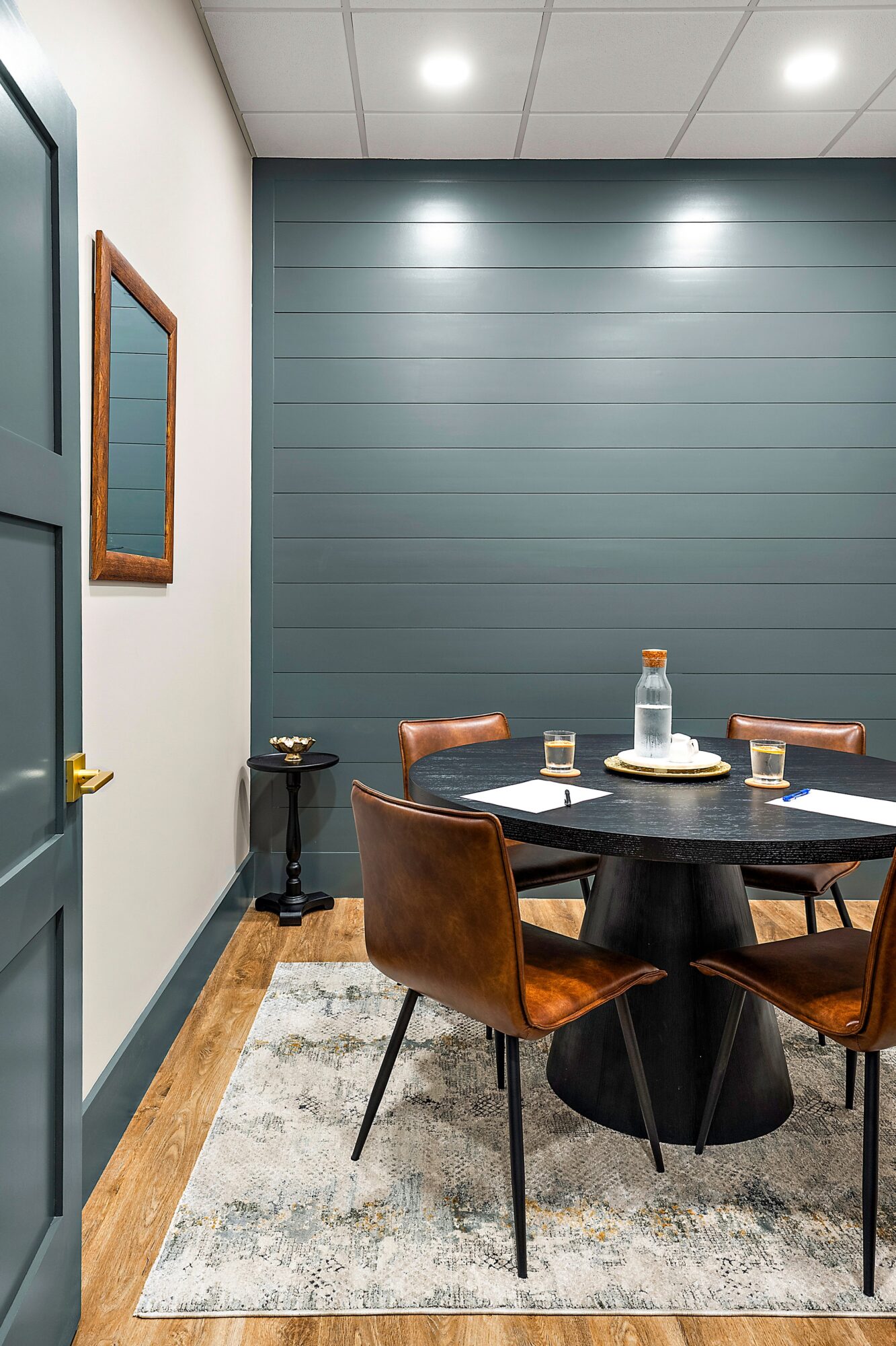 Round table with four chairs, cake, and drinks in a room with blue wall and wooden floor.