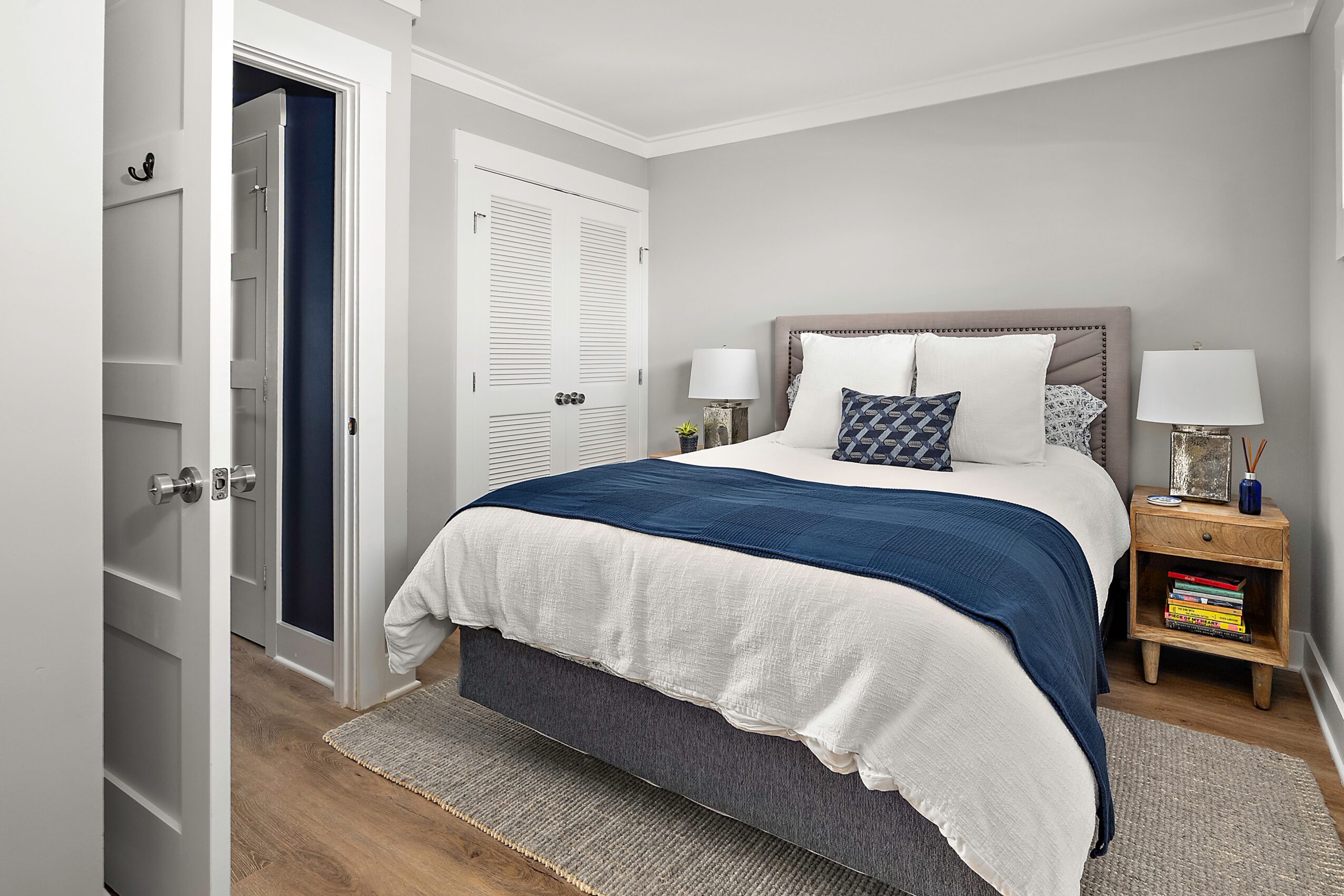 Bedroom with bed, two nightstands, lamps, and closed closet doors, in a neutral color scheme.