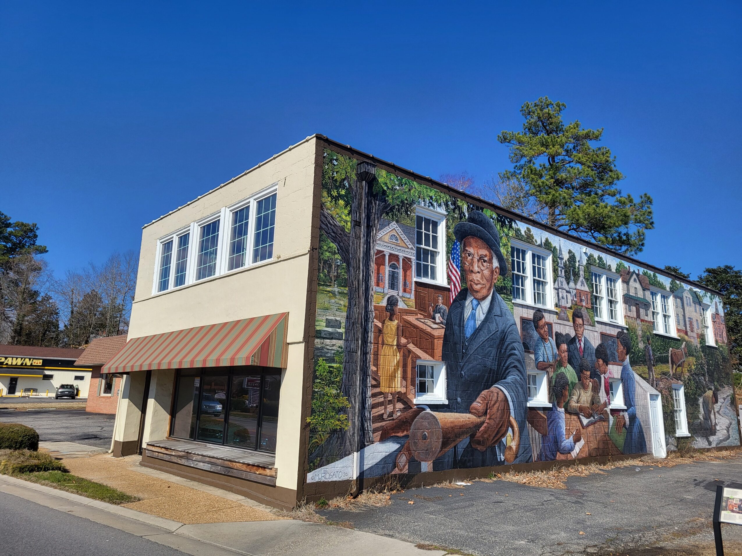 Building with a mural of children and adults sitting outdoors, blue sky, and trees in background.