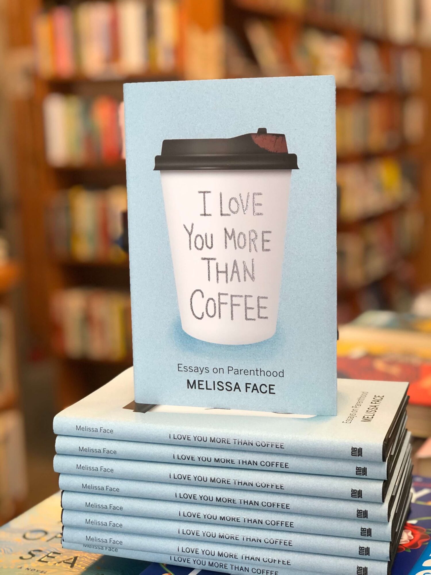 Book with a coffee cup illustration and handwritten message, on a table in a bookstore, with shelves in the background.
