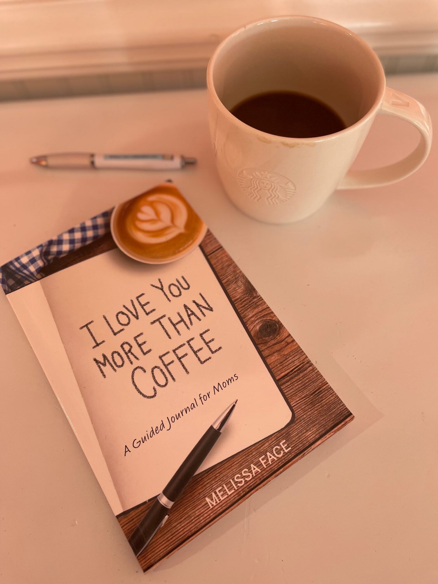 A notebook with a handwritten message, a pen, a cookie, a coffee mug, and a pen on a wooden surface.