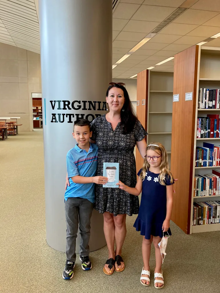 Woman with two children in a library, holding a book, bookshelves in background.