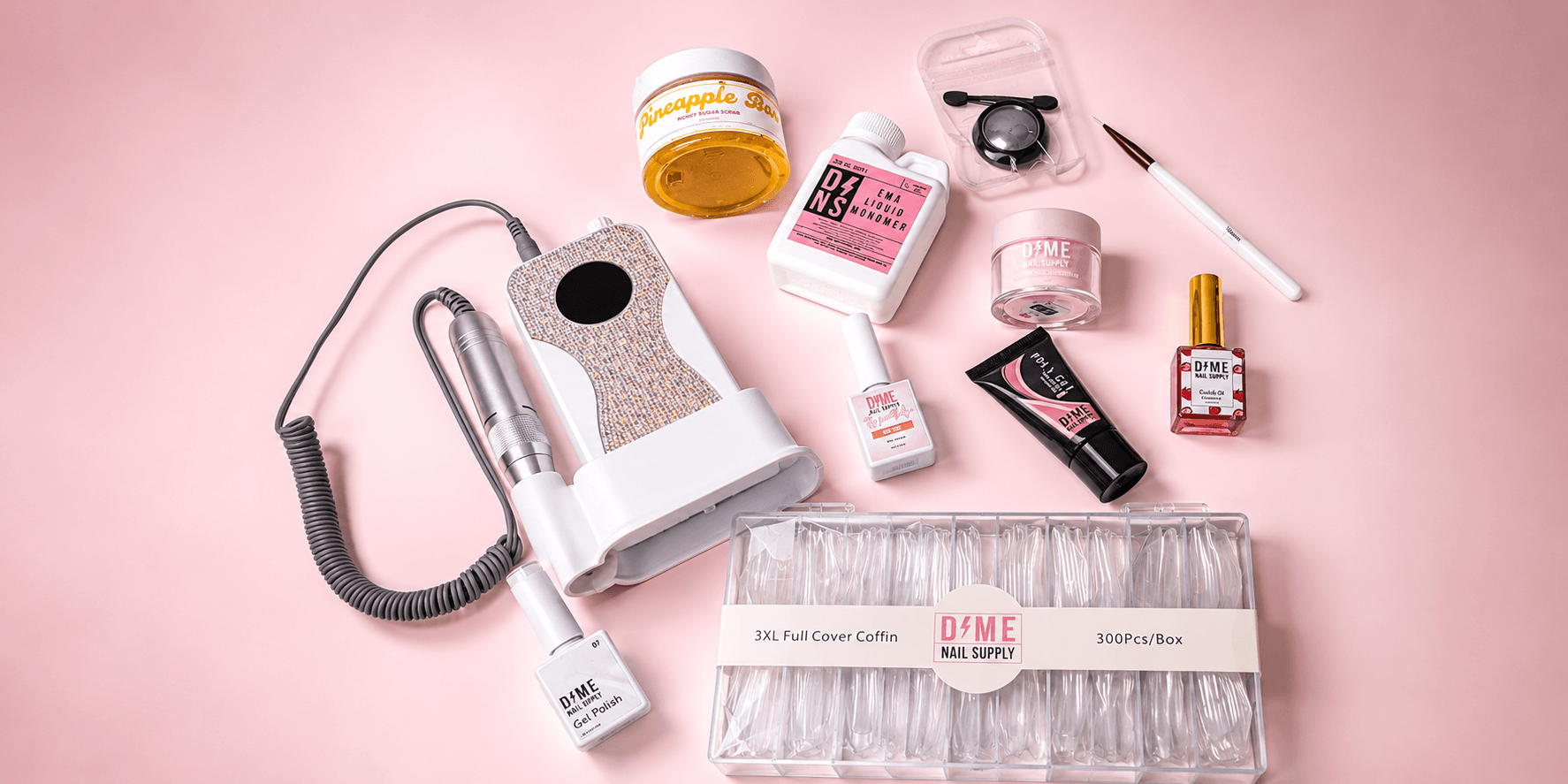 Various skincare and beauty products arranged on a pink background, including a device, jars, bottles, and a dropper.