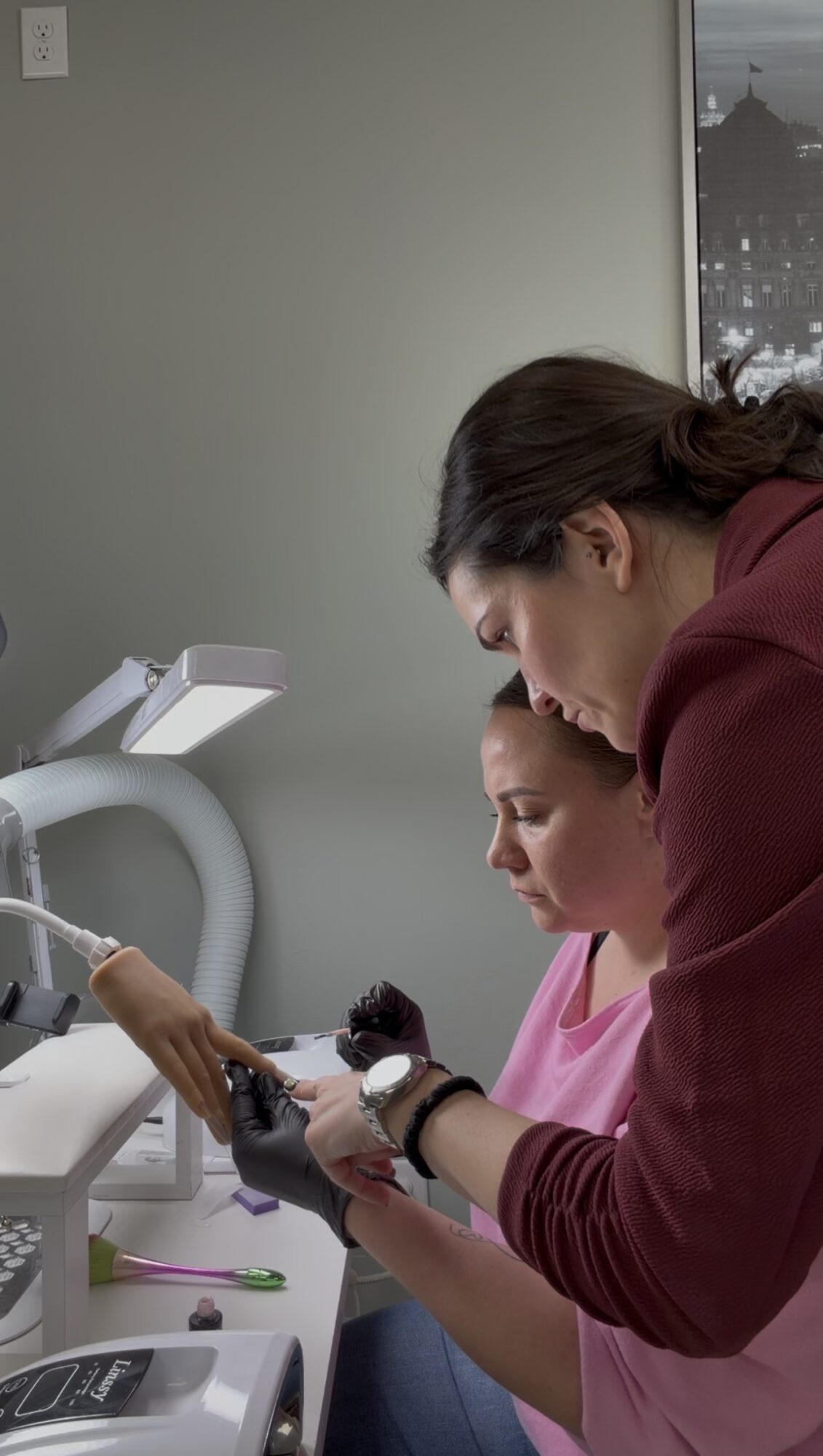 A woman in a maroon shirt assists a young girl in a pink shirt with a medical device, in a clinical setting.