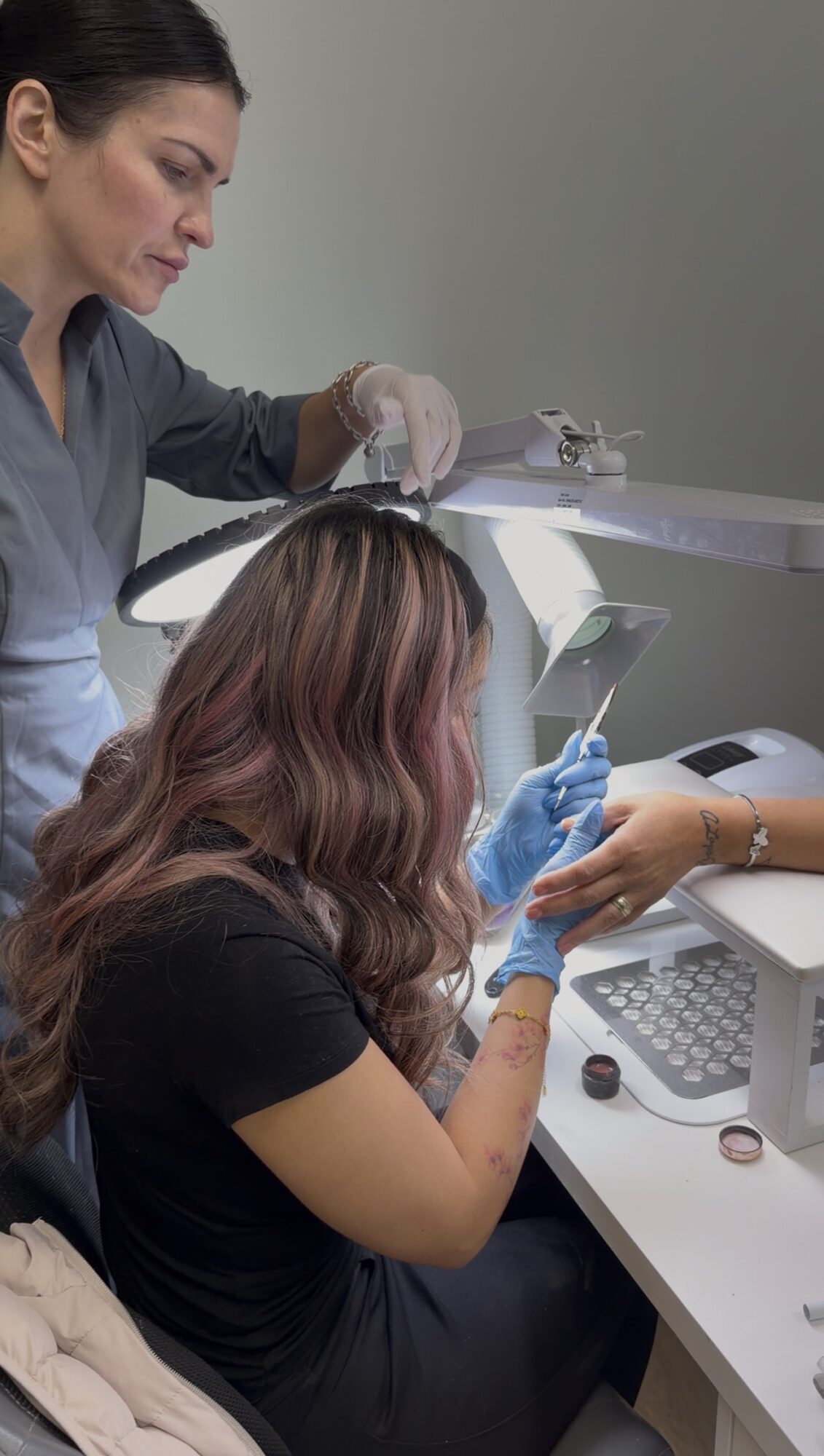 Two women working with a medical or laboratory device, one standing and one sitting, in a clinical setting.