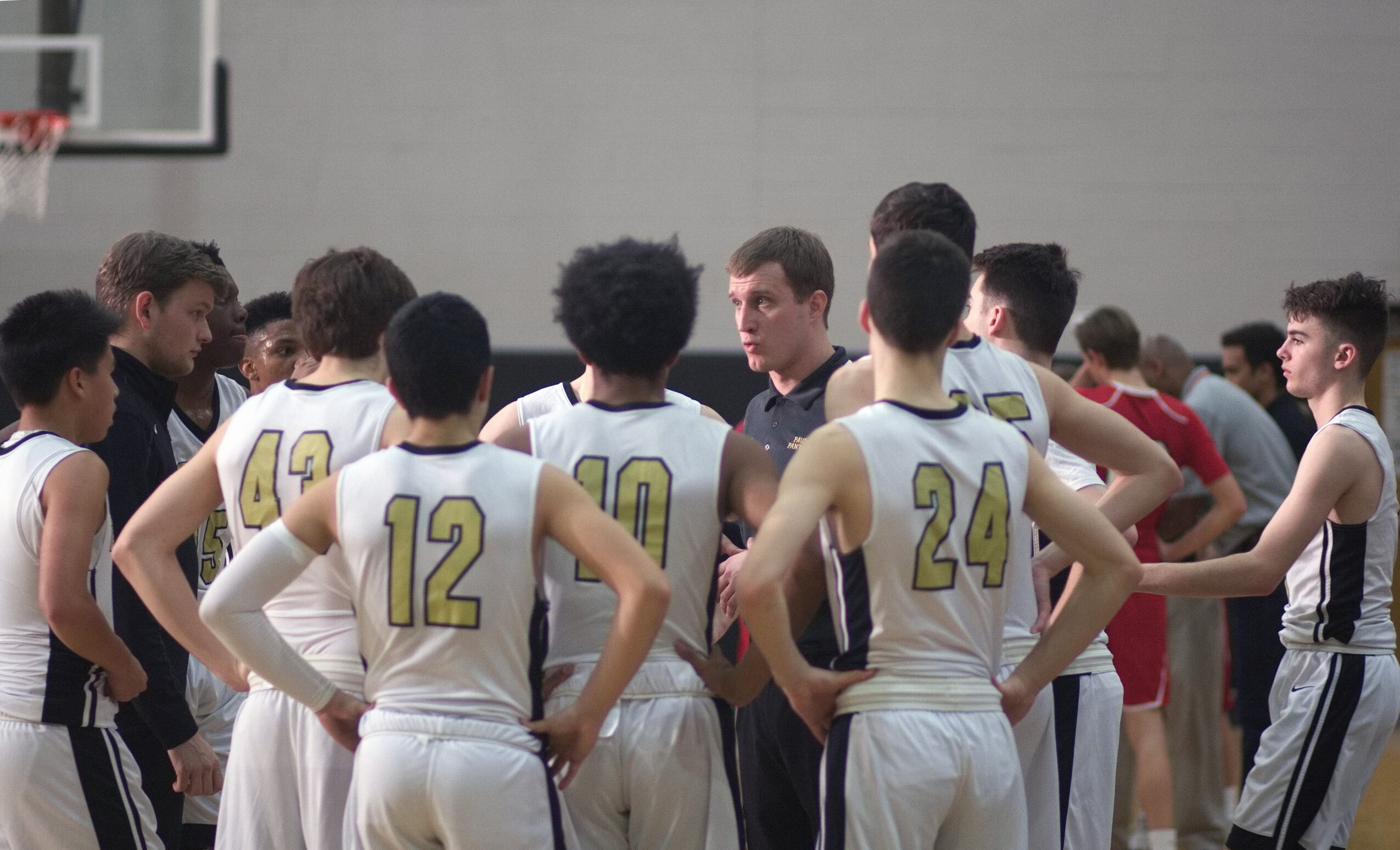 Group of basketball players in white jerseys with yellow numbers, gathered around a coach in a gymnasium.